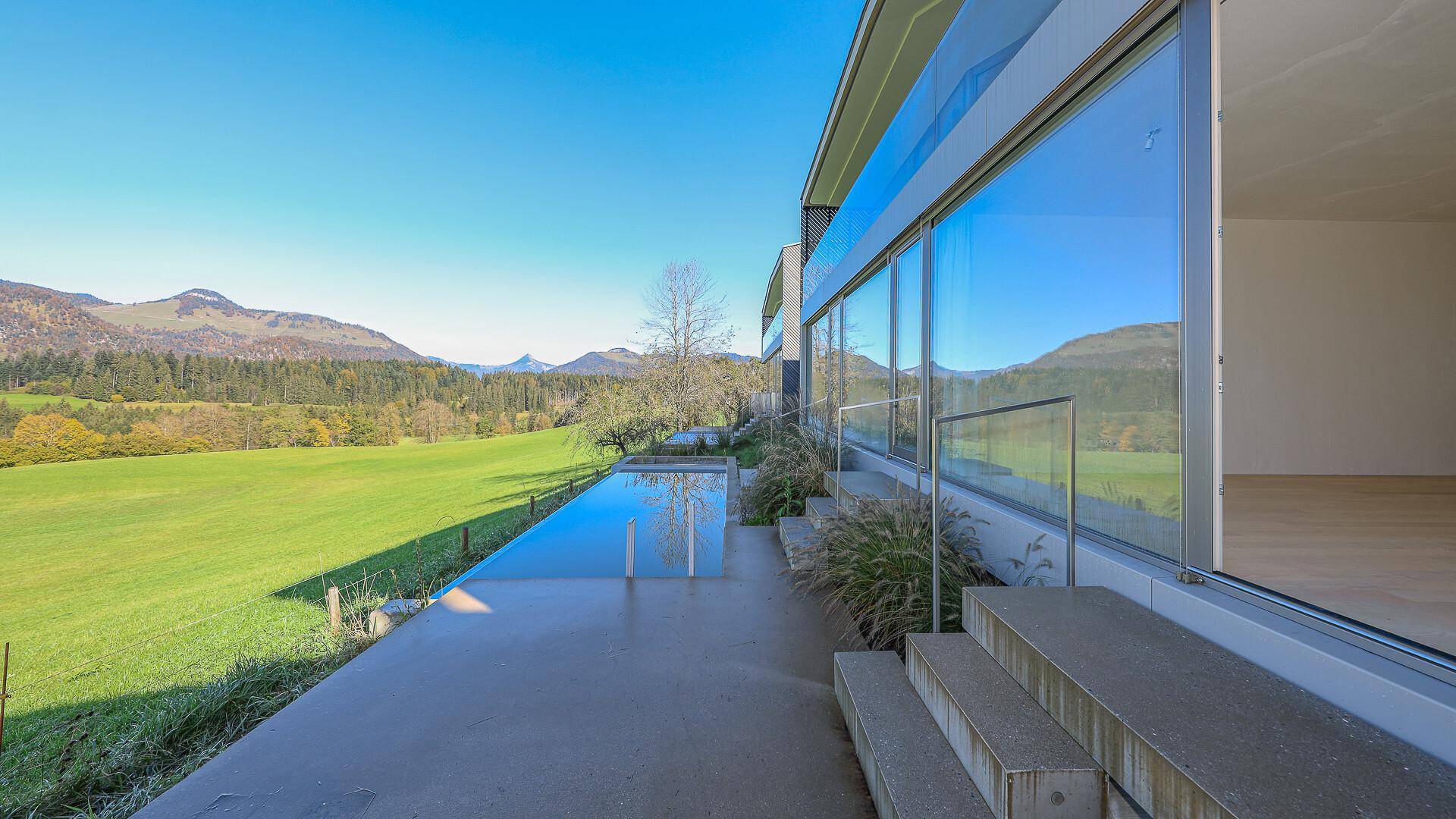 Terrassenbereich am Pool mit weitem Blick auf die grüne Landschaft und die Berge.