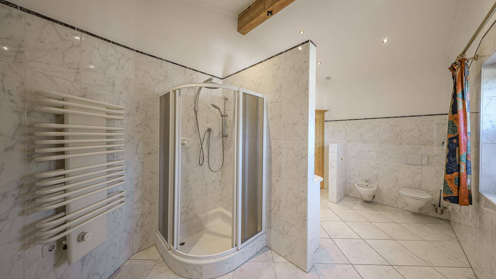 Traditionelles Badezimmer mit Eckdusche, WC, Bidet und beheiztem Handtuchhalter.