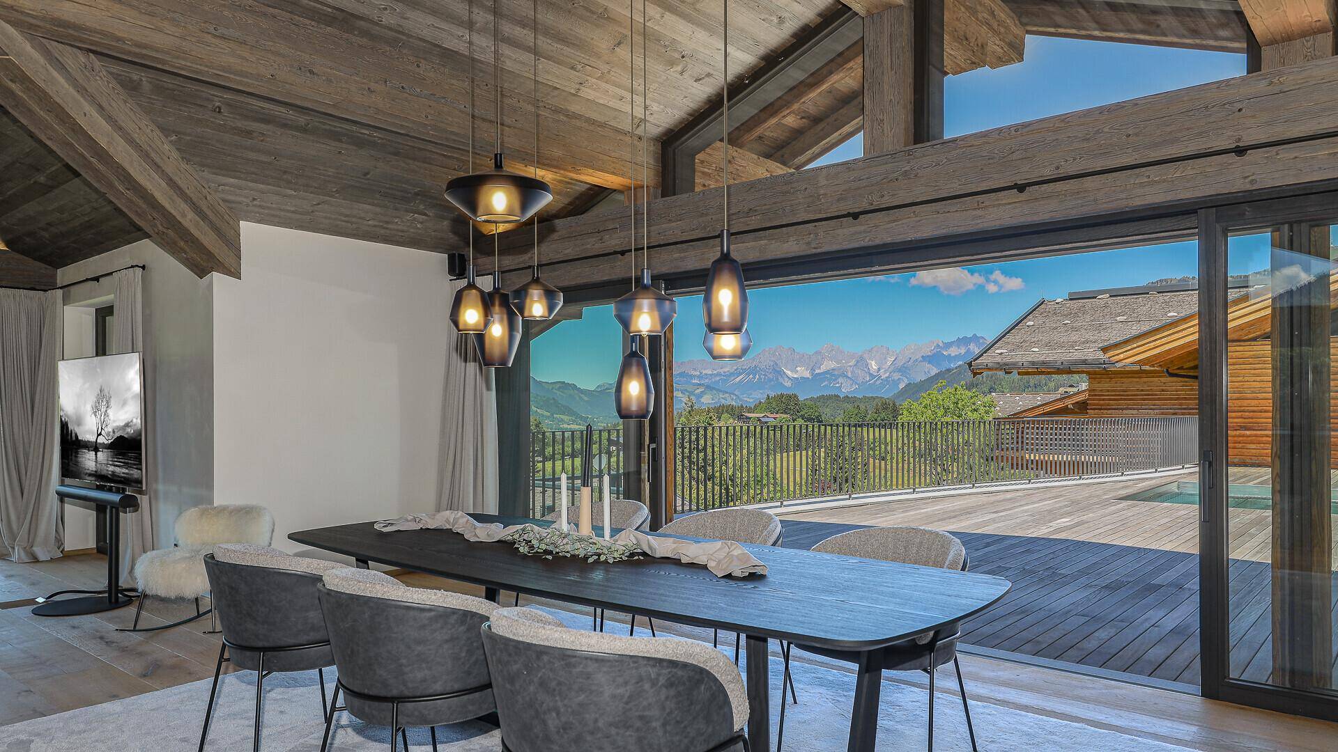 Eleganter Essbereich mit modernem Tisch, Pendelleuchten und Panoramablick auf die Alpen.