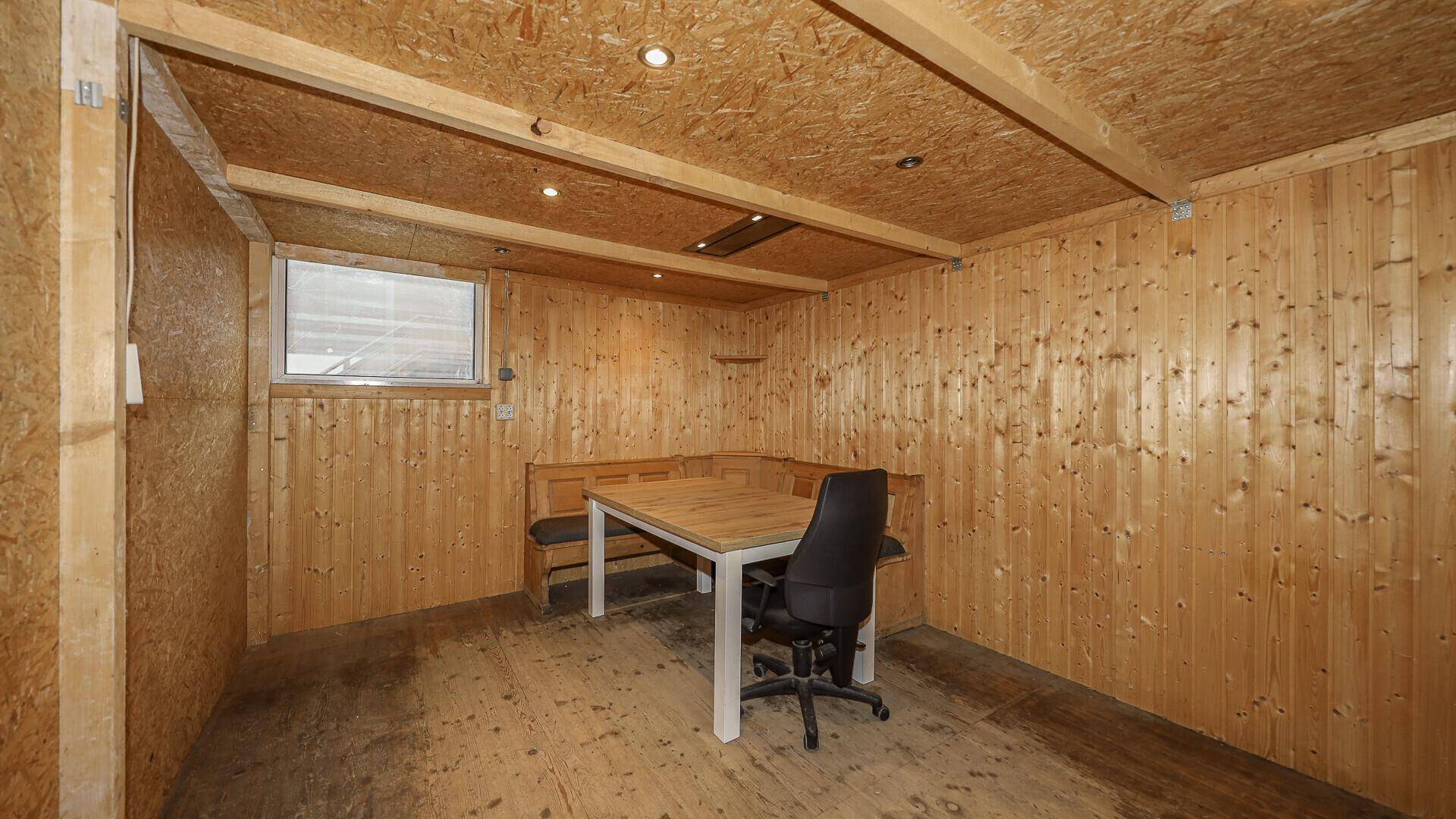 Kleiner, holzvertäfelter Raum mit einem Tisch, Stühlen und einem Fenster, ideal als Büro oder Aufenthaltsraum.