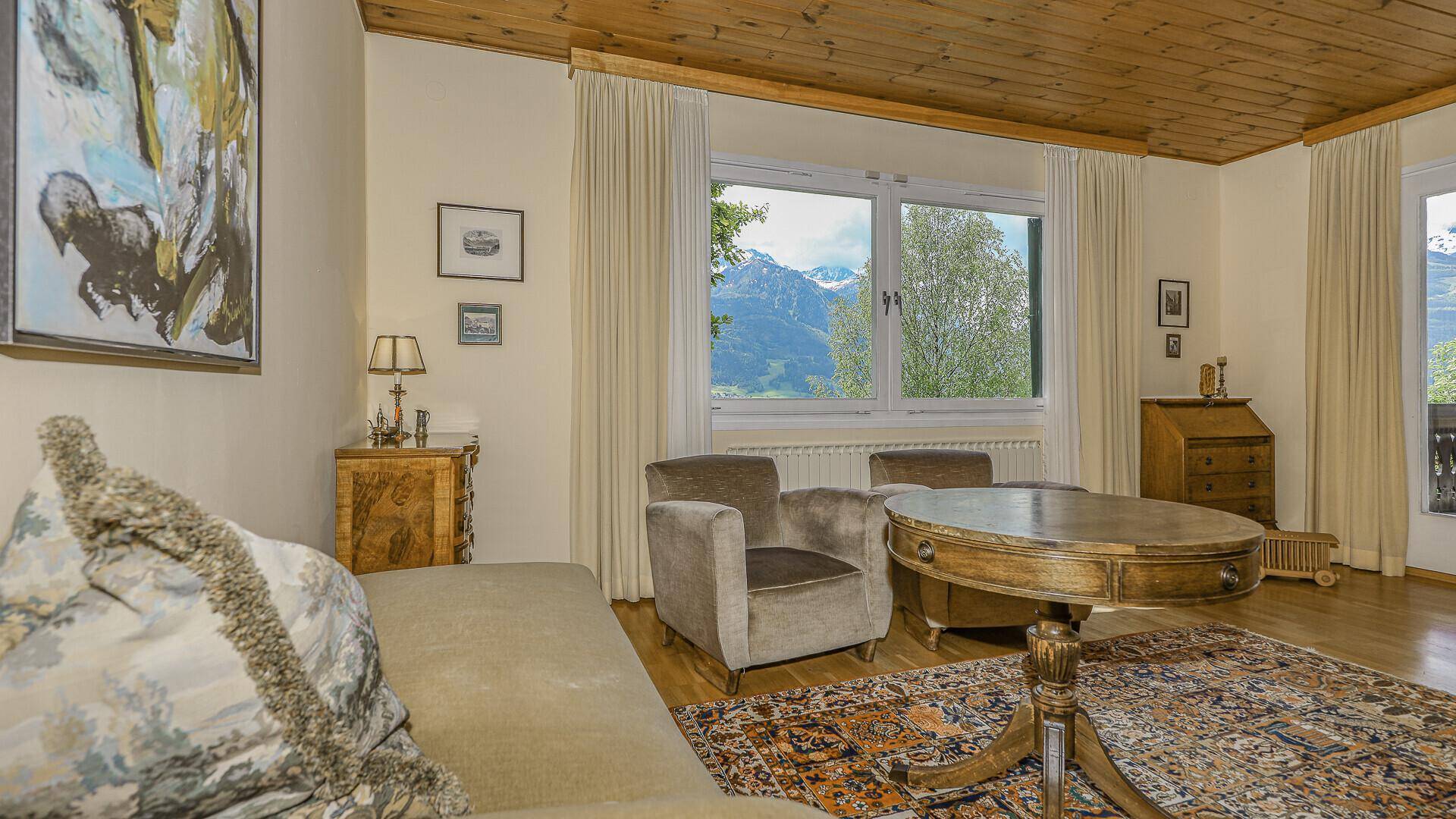 Detailansicht des Wohnzimmers mit Holztisch, Sesseln und Bergblick durch das große Fenster.
