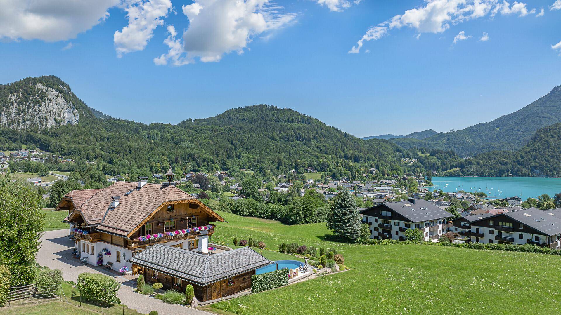 Panoramablick auf ein Anwesen mit traditioneller Architektur, Pool und See- und Bergblick.