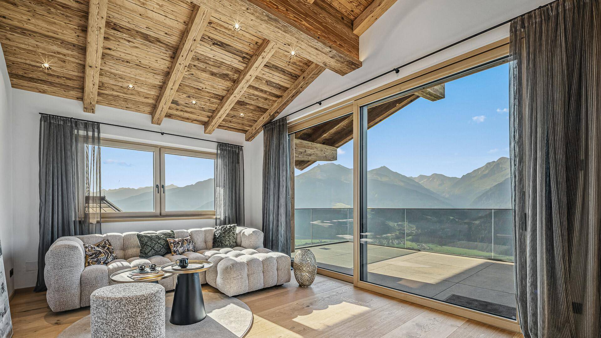 Gemütliches Wohnzimmer mit großem Sofa, Holzbalkendecke und Zugang zur Terrasse mit Bergblick.