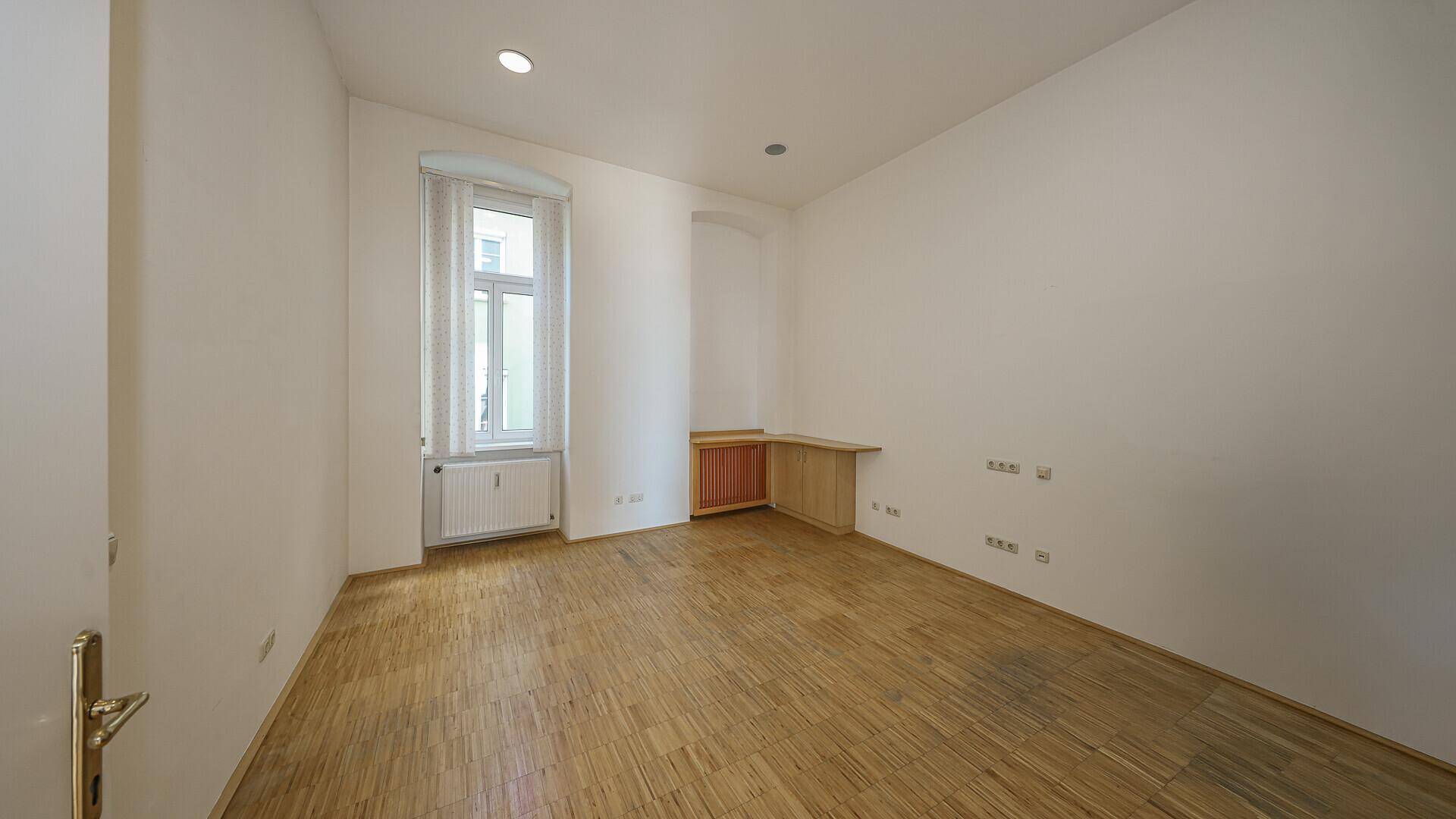Heller, leerer Raum mit Holzparkett und großem Fenster, bereit zur individuellen Gestaltung.