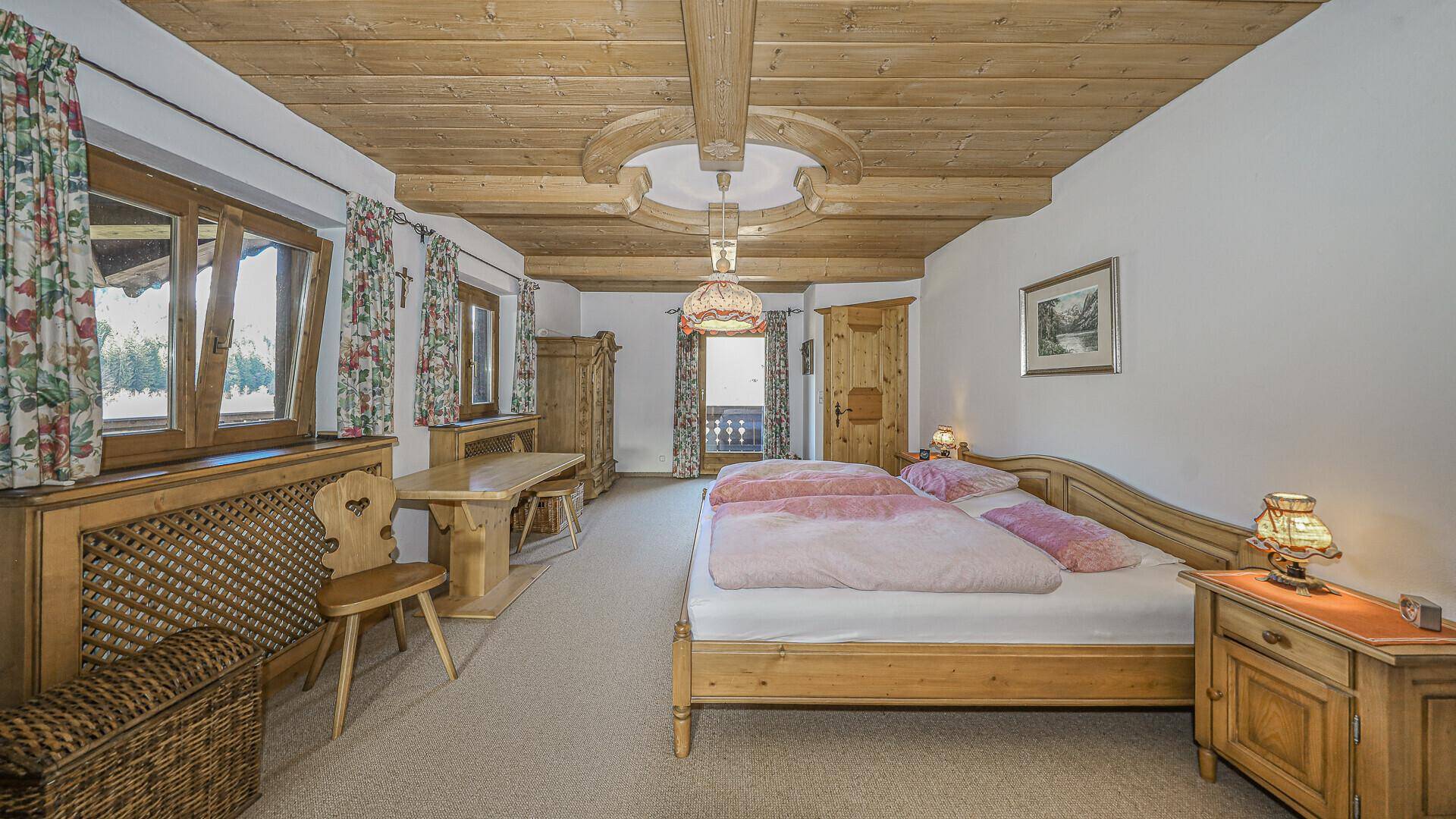 Gemütliches Schlafzimmer im alpenländischen Stil mit Holzdecke, Doppelbett und Blick ins Grüne.