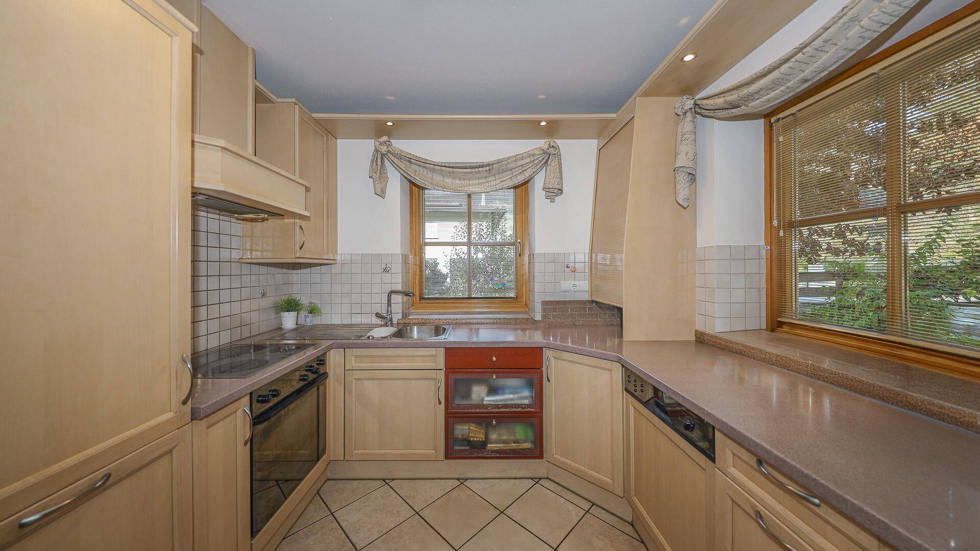 Funktionale Küche im Landhausstil mit beigen Schränken, Fliesenboden und Fenster.