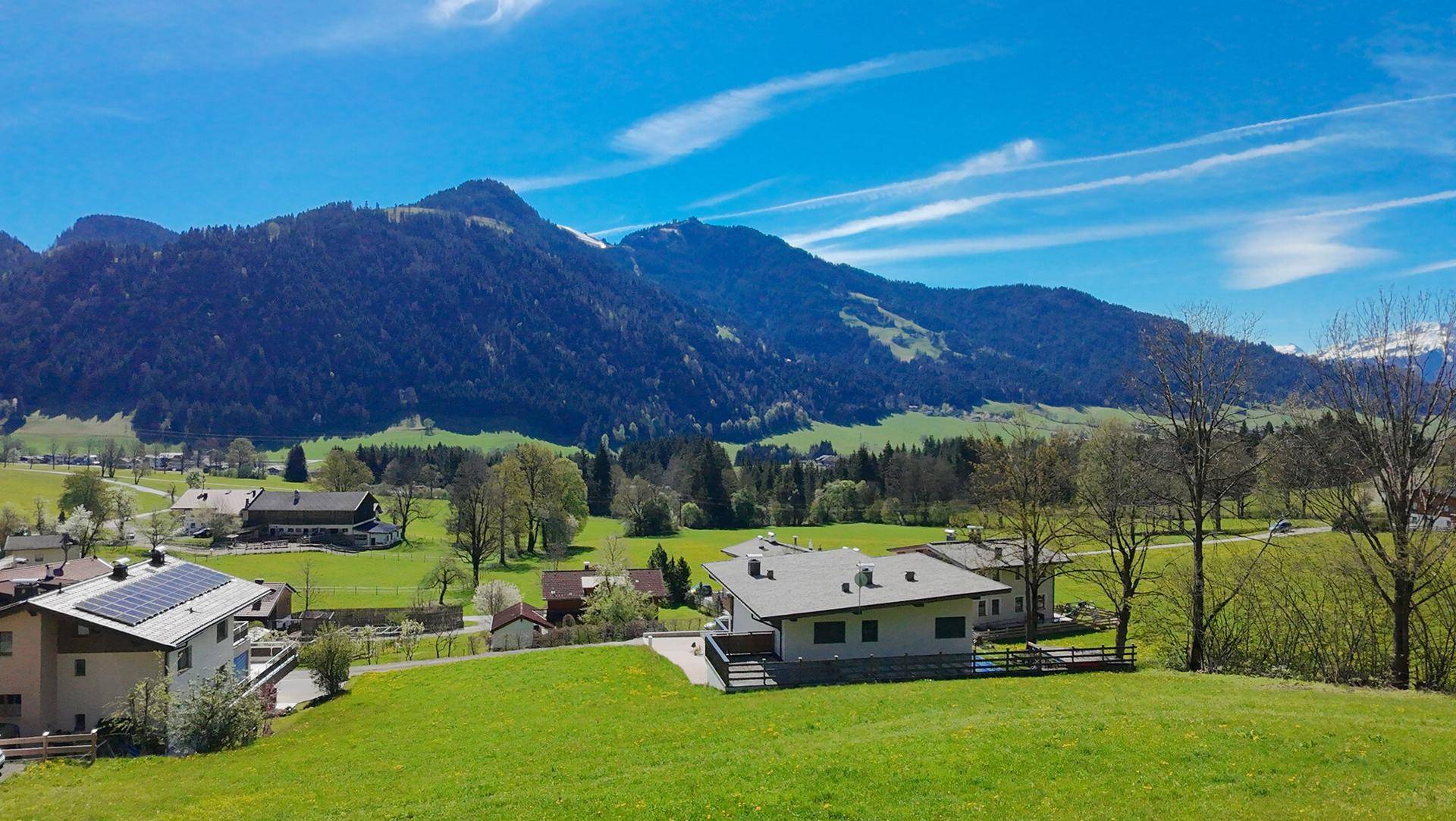 Idyllische Ansicht von Häusern in einer weiten grünen Landschaft mit schneebedeckten Berggipfeln.