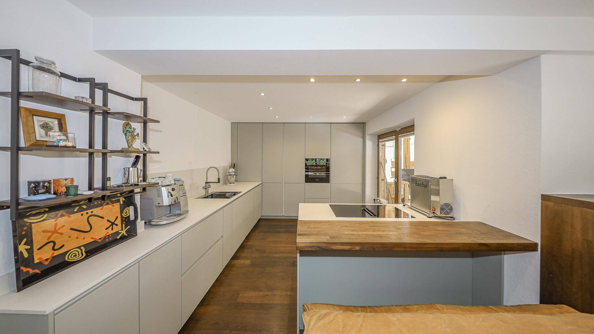 Moderne Einbauküche mit hellgrauen Fronten, Holztheke und integrierten Geräten.