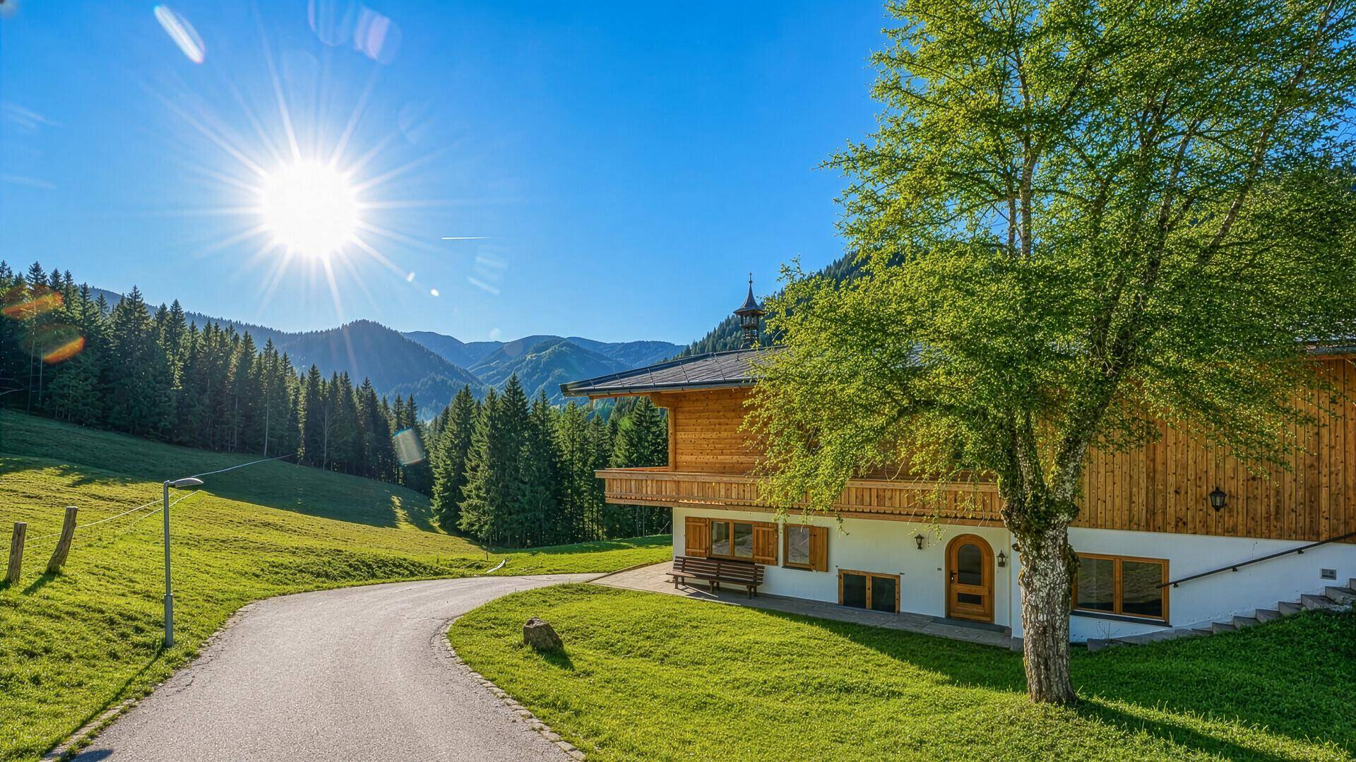 Idyllisches Holzchalet mit Zufahrt, umgeben von grünen Wiesen und Bergen unter strahlendem Sonnenschein.