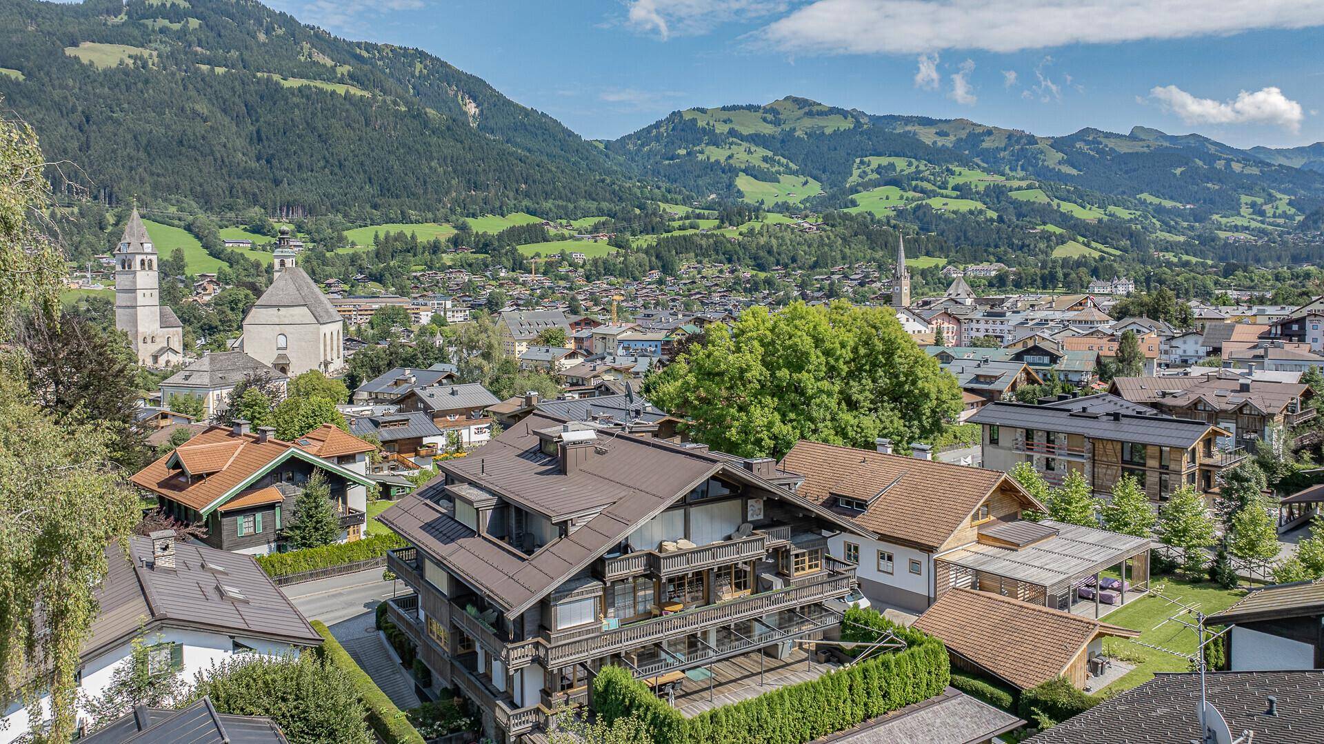 Luftaufnahme einer charmanten Stadt in den Alpen mit traditionellen Gebäuden und grünen Bergen im Hintergrund.