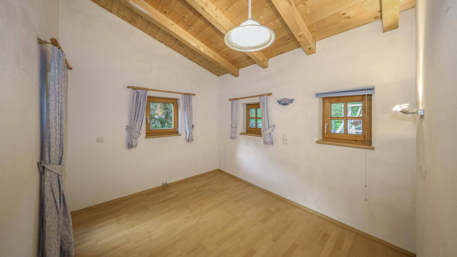 Helles Schlafzimmer mit Holzbalkendecke und mehreren Fenstern, bietet eine ruhige Atmosphäre.