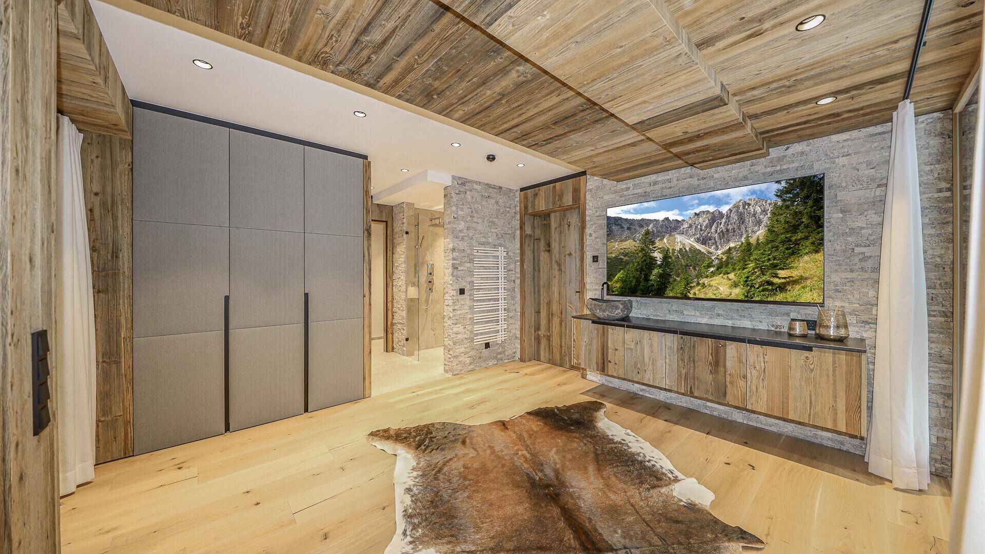 Schlafzimmer mit Holzboden, Einbauschränken und großem Fernseher mit Bergbild.