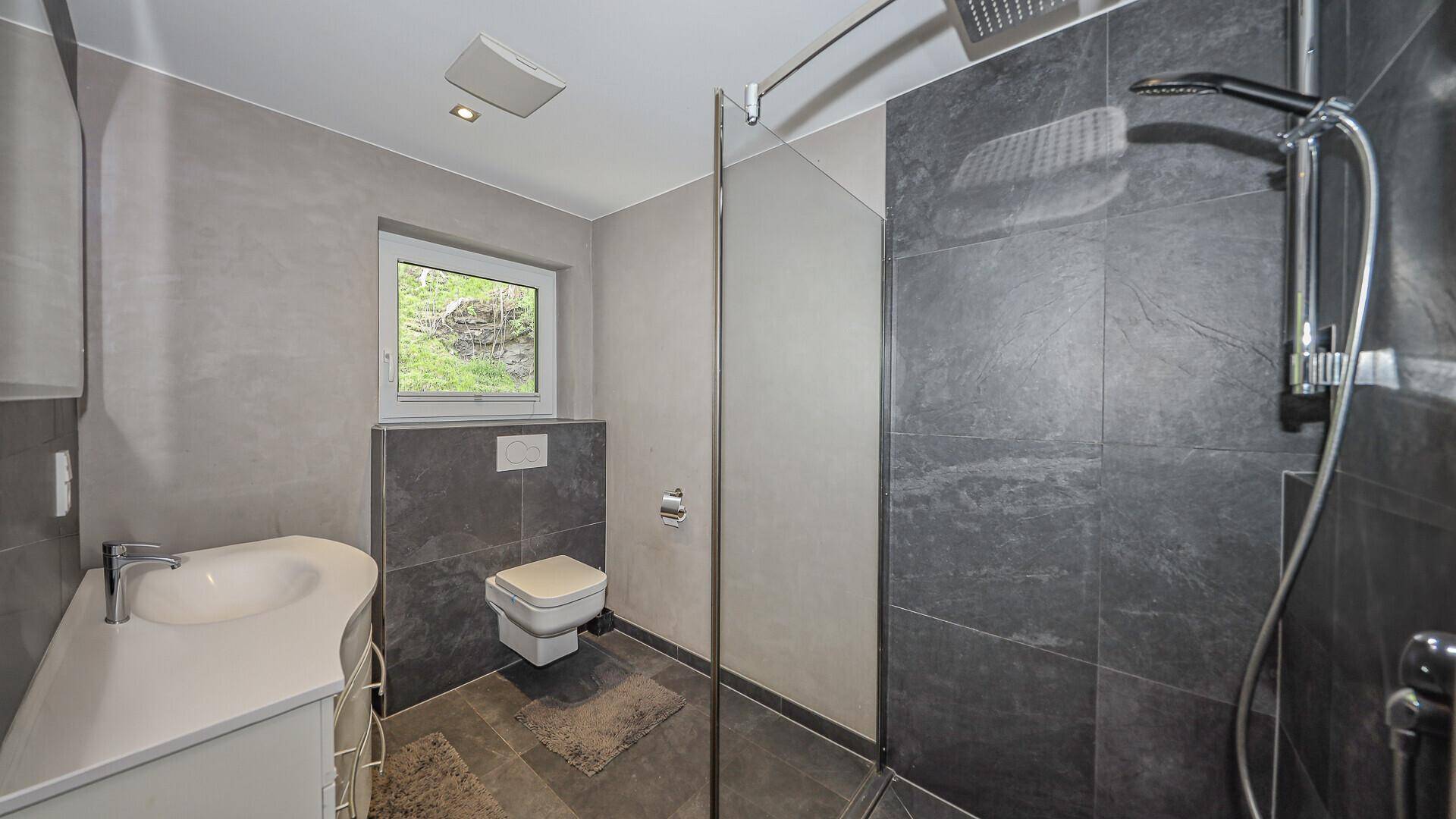 Geräumige Duschkabine mit Regendusche und modernem Waschtisch in grau gefliestem Bad.
