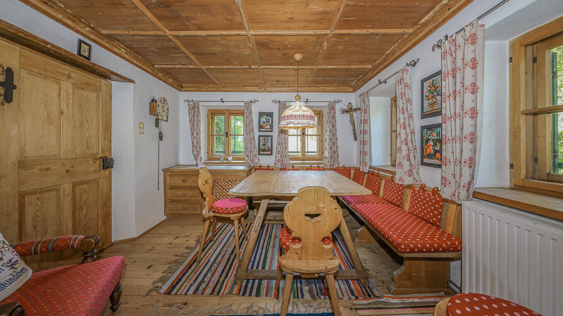 Traditioneller Essbereich mit Holztisch, Eckbank und karierten Vorhängen im Originalzustand.