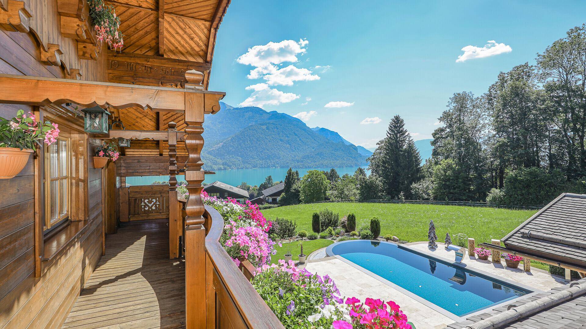 Geräumiger Holzbalkon mit Blumen und weitem Blick auf den See, die Berge und den Poolbereich.