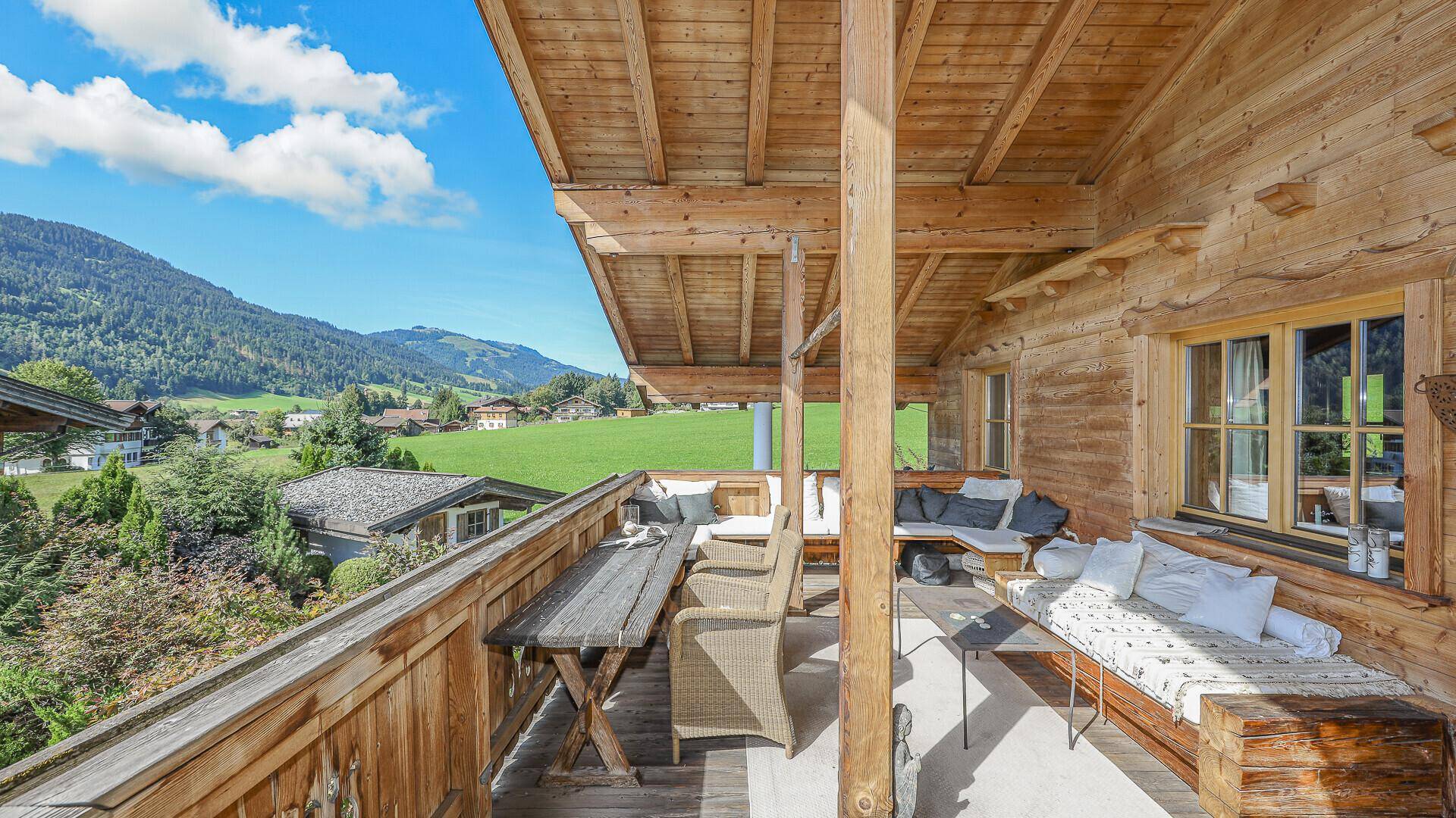 Geräumiger Holzbalkon mit Essbereich und weitem Blick über grüne Hügel und Berge.