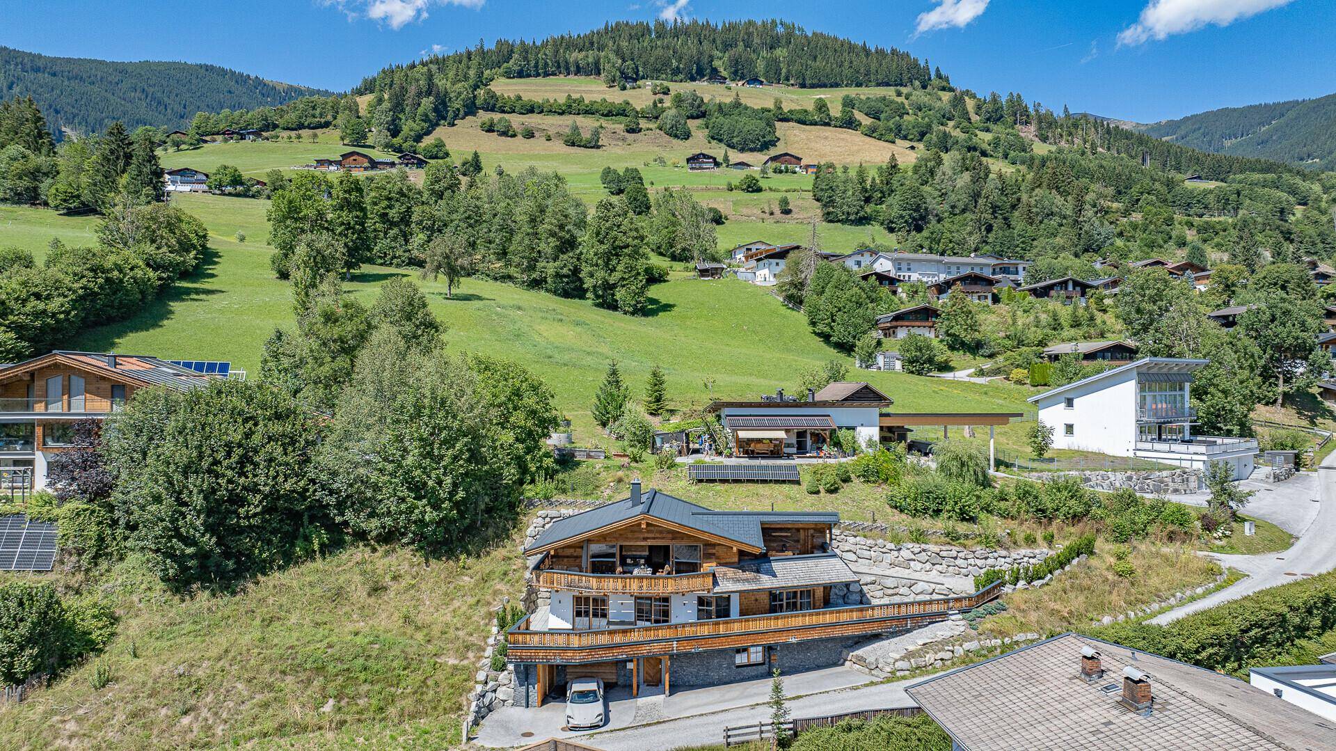 Luftaufnahme eines charmanten Chalets in einer grünen Berglandschaft.