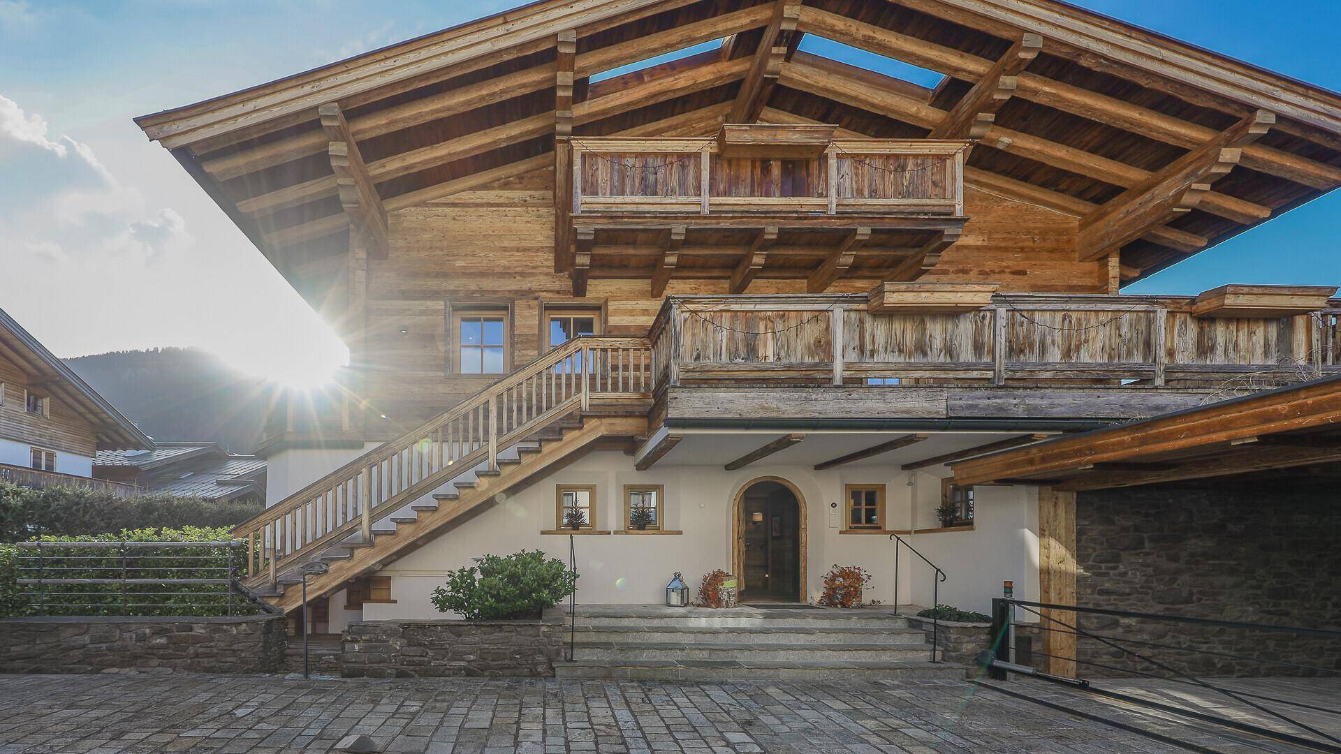 Eingangsbereich des Holzchalets mit Außentreppe, Balkonen und sonniger Ausrichtung.