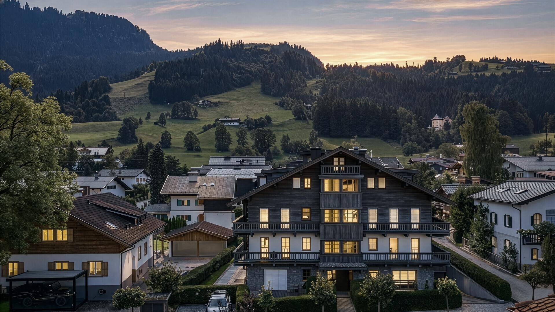 Abendansicht eines traditionellen Gebäudes mit beleuchteten Fenstern und Bergblick bei Sonnenuntergang.