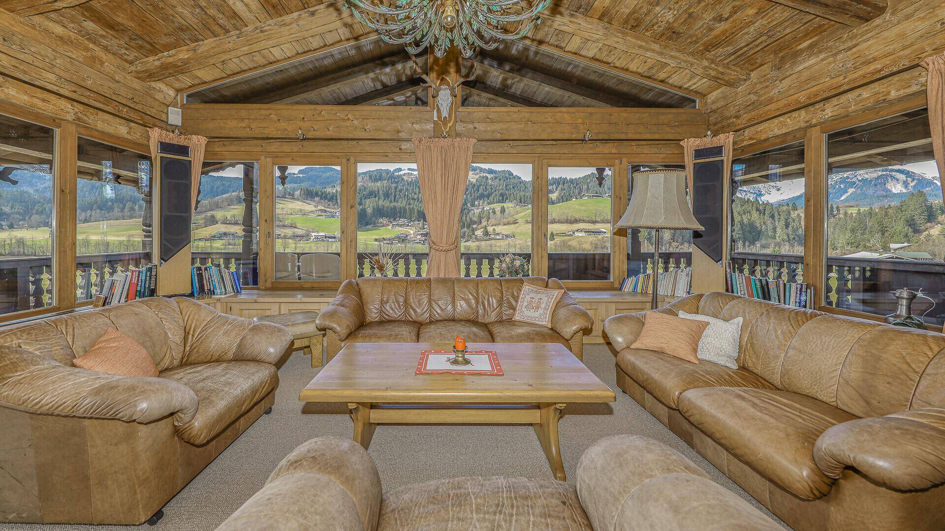 Gemütliches Wohnzimmer im alpenländischen Stil mit Ledersofas, Holzbalkendecke und weitem Bergblick.