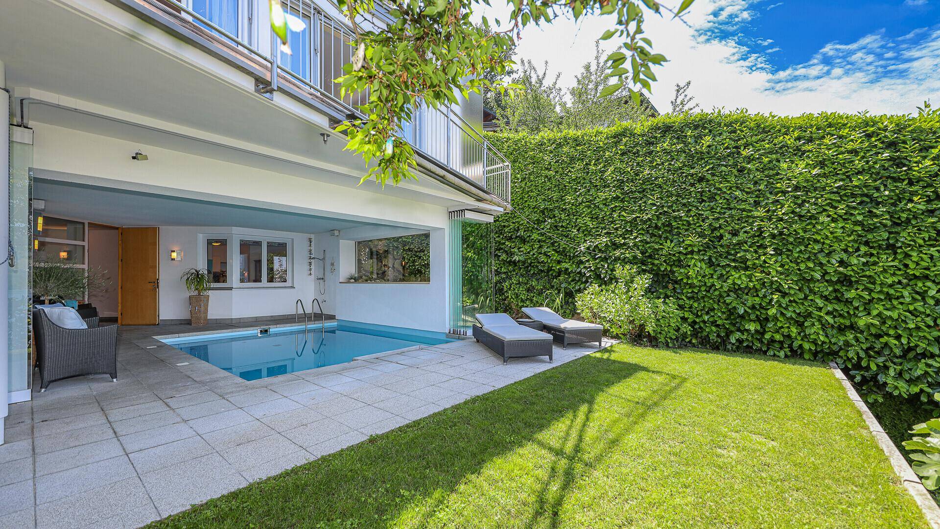 Gepflegter Garten mit Rasenfläche, Pool und Liegestühlen, umgeben von einer hohen Hecke.