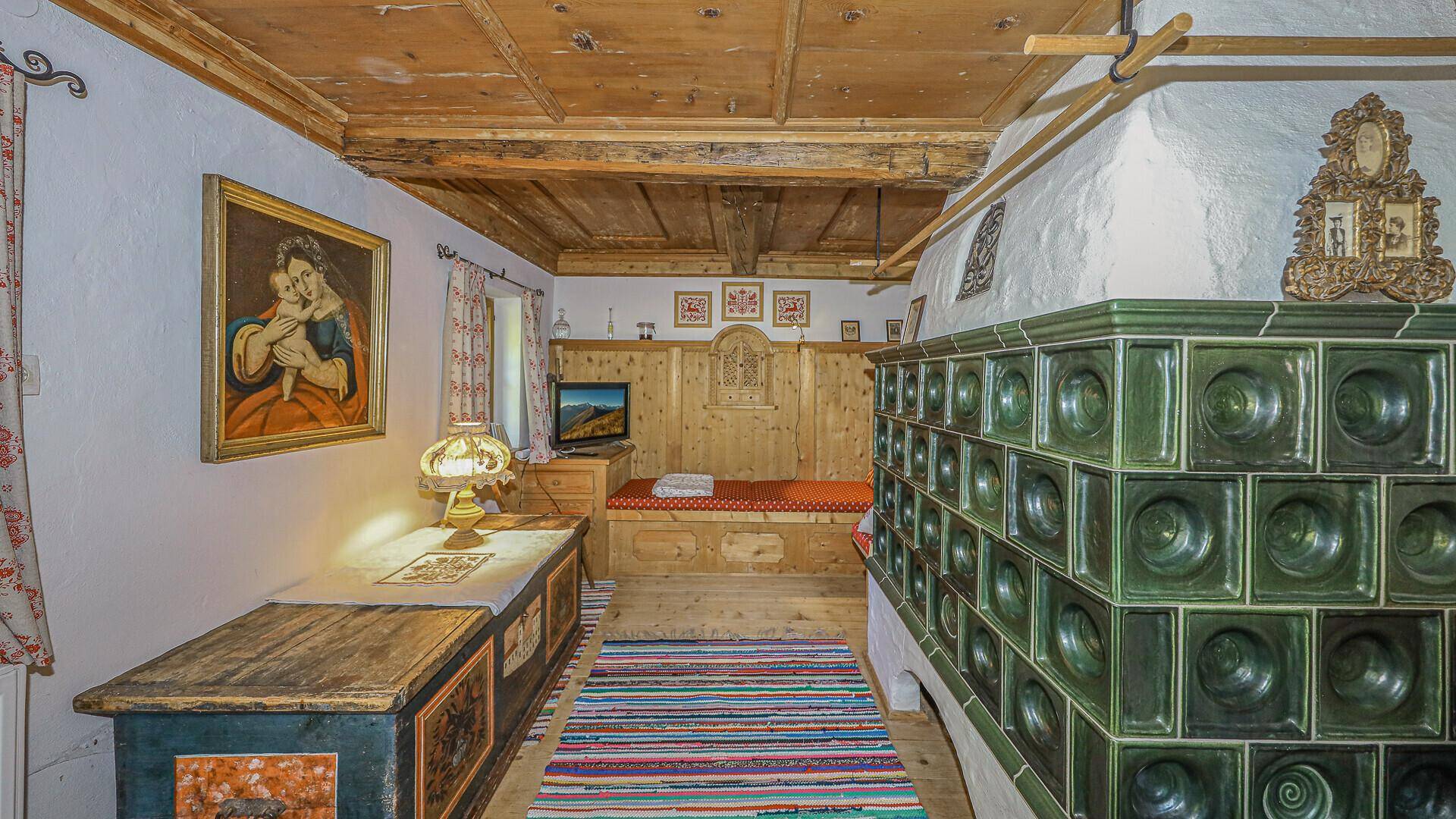 Traditionelles Schlafzimmer mit Kachelofen, Holzbett und rustikalen Möbeln im Originalzustand.