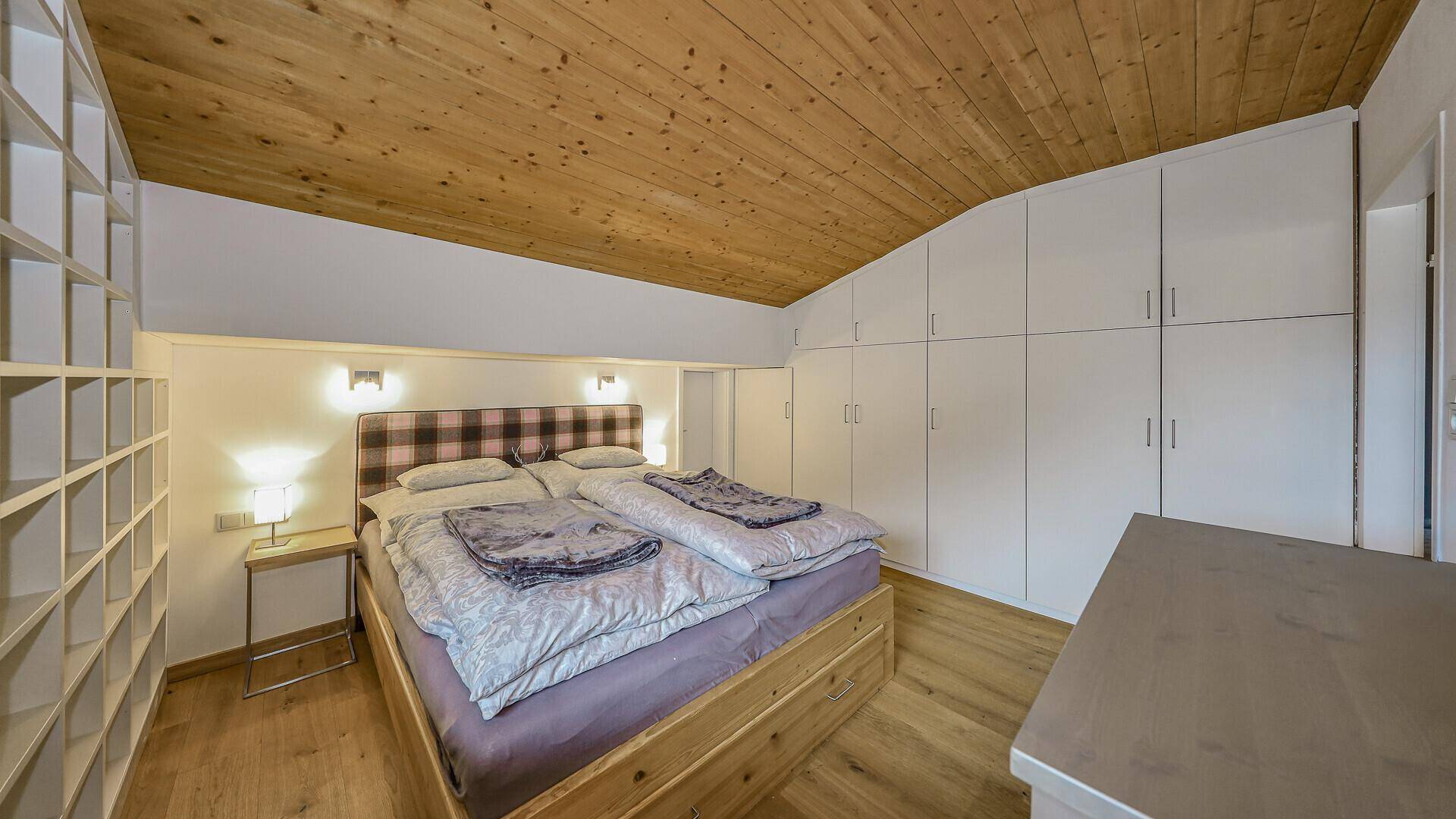 Gemütliches Schlafzimmer mit Doppelbett, weißen Einbauschränken und Holzdecke unter Dachschräge.
