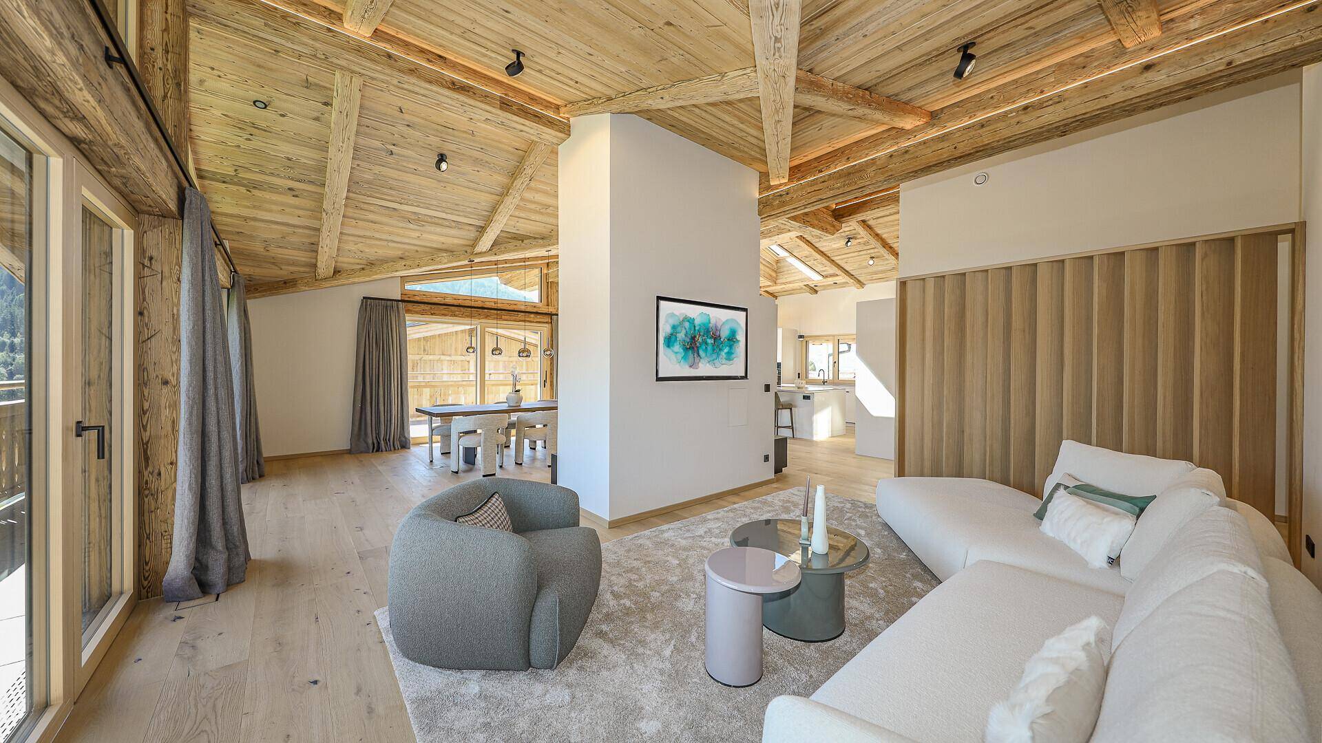 Gemütlicher Wohnbereich mit modernem Sofa, Teppich und Holzwänden, offen zum Essbereich.