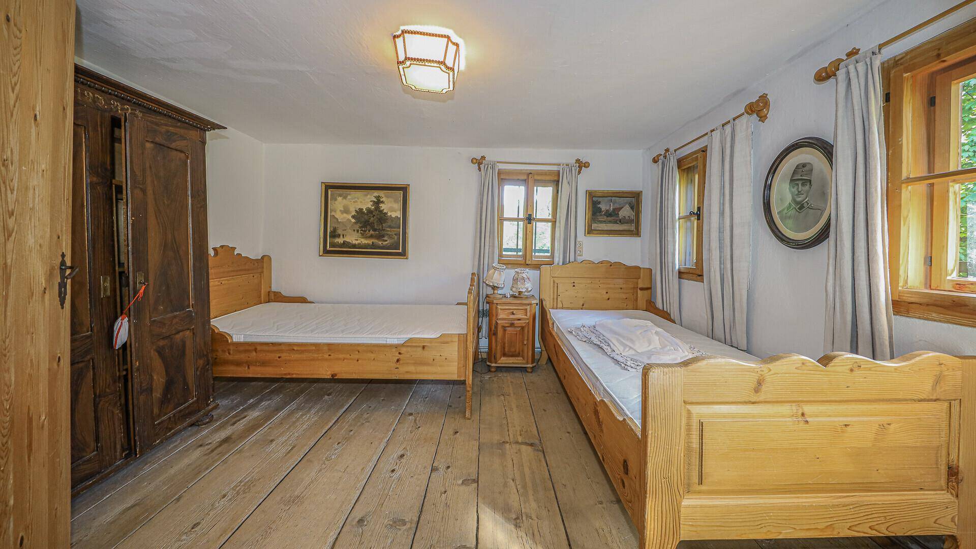 Schlafzimmer im Originalzustand mit zwei Einzelbetten, Holzschrank und Holzboden.