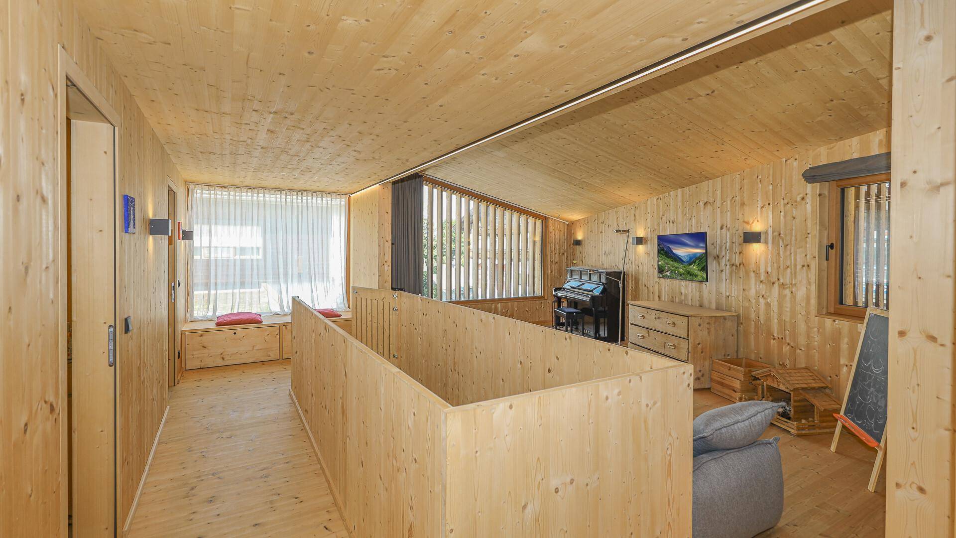 Offener Wohnbereich mit Klavier, bequemen Sofas und Holzwänden, ideal für Musik und Entspannung.