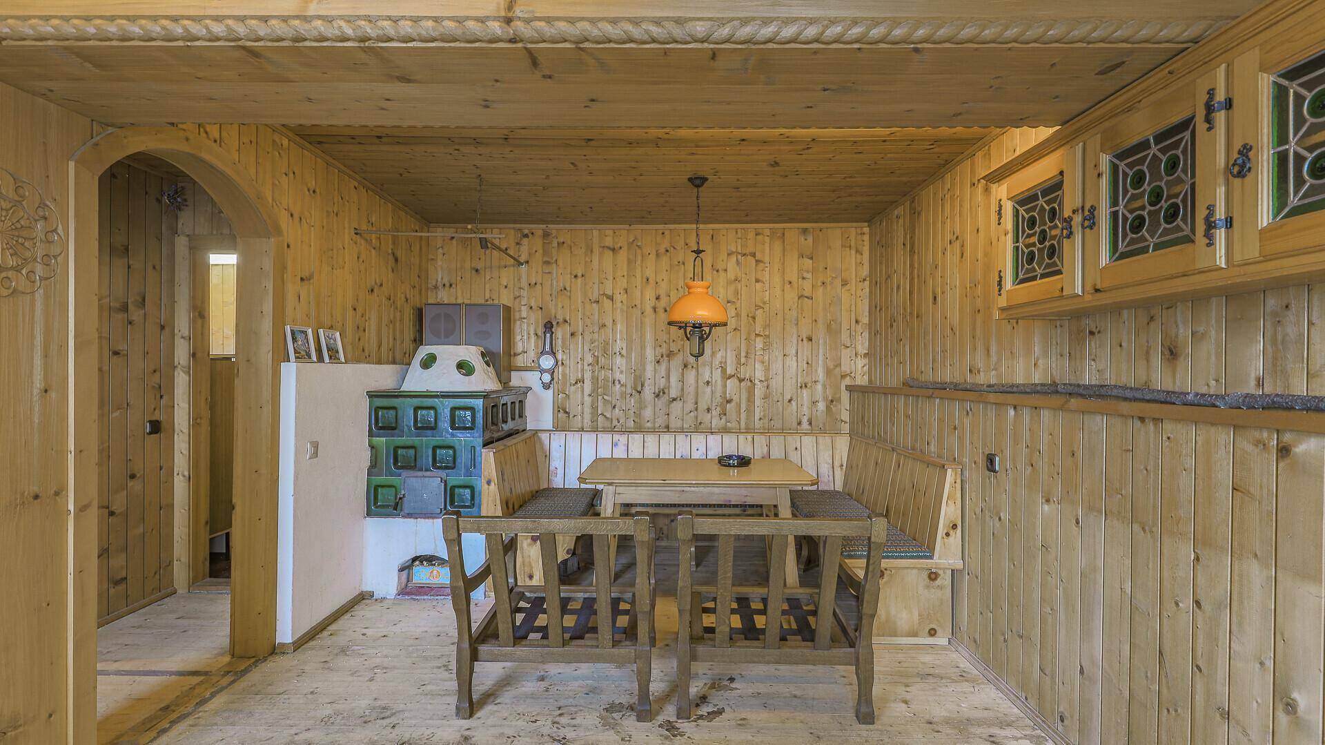 Rustikaler Essbereich mit Holzwänden, Eckbank und traditionellem Kachelofen.