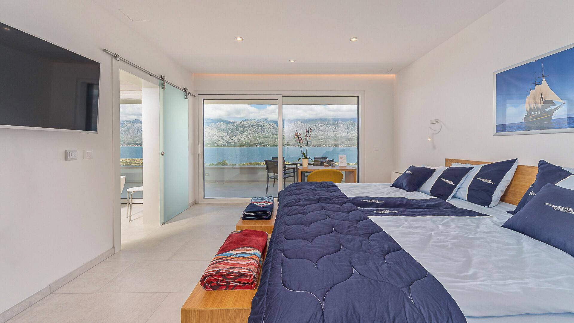 Helles Schlafzimmer mit Doppelbett, Schiebetür zur Terrasse und weitem Blick auf das Meer und die Berge.