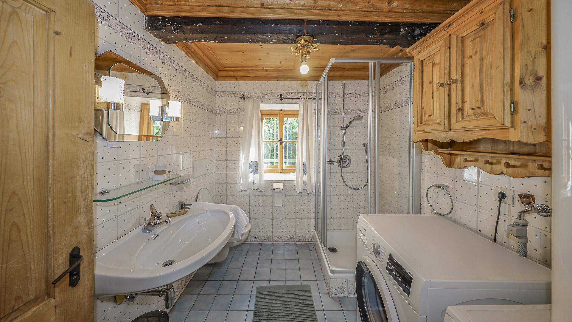 Traditionelles Badezimmer im Originalzustand mit Duschkabine, Waschbecken und Waschmaschine.