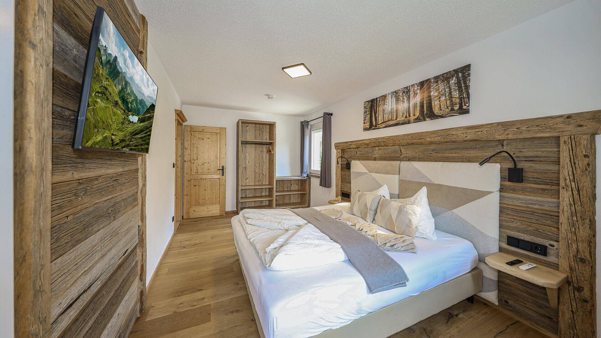 Gemütliches Schlafzimmer mit Doppelbett, Holzelementen und einem Wandfernseher.