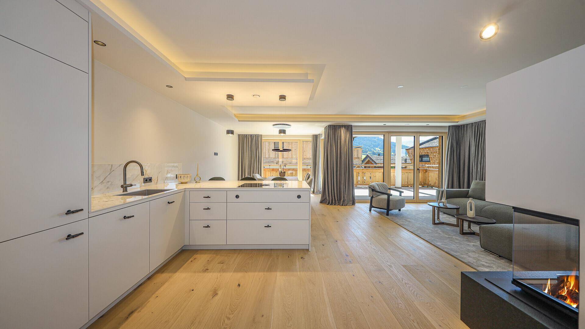 Offener Wohnbereich mit moderner Küche, Kamin und Zugang zu einem großen Balkon.