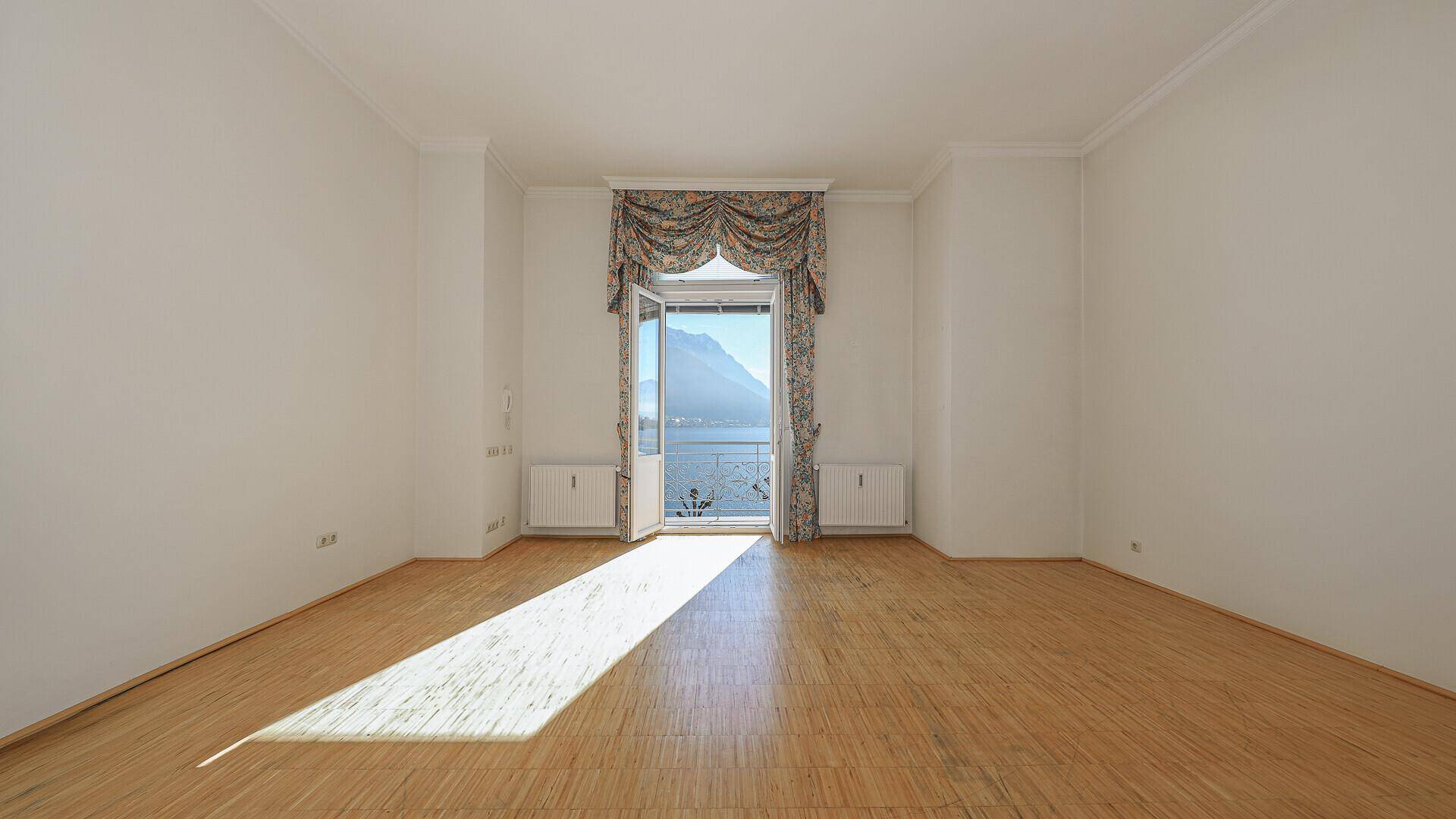 Heller, leerer Raum mit Parkettboden und französischem Balkon mit Seeblick.