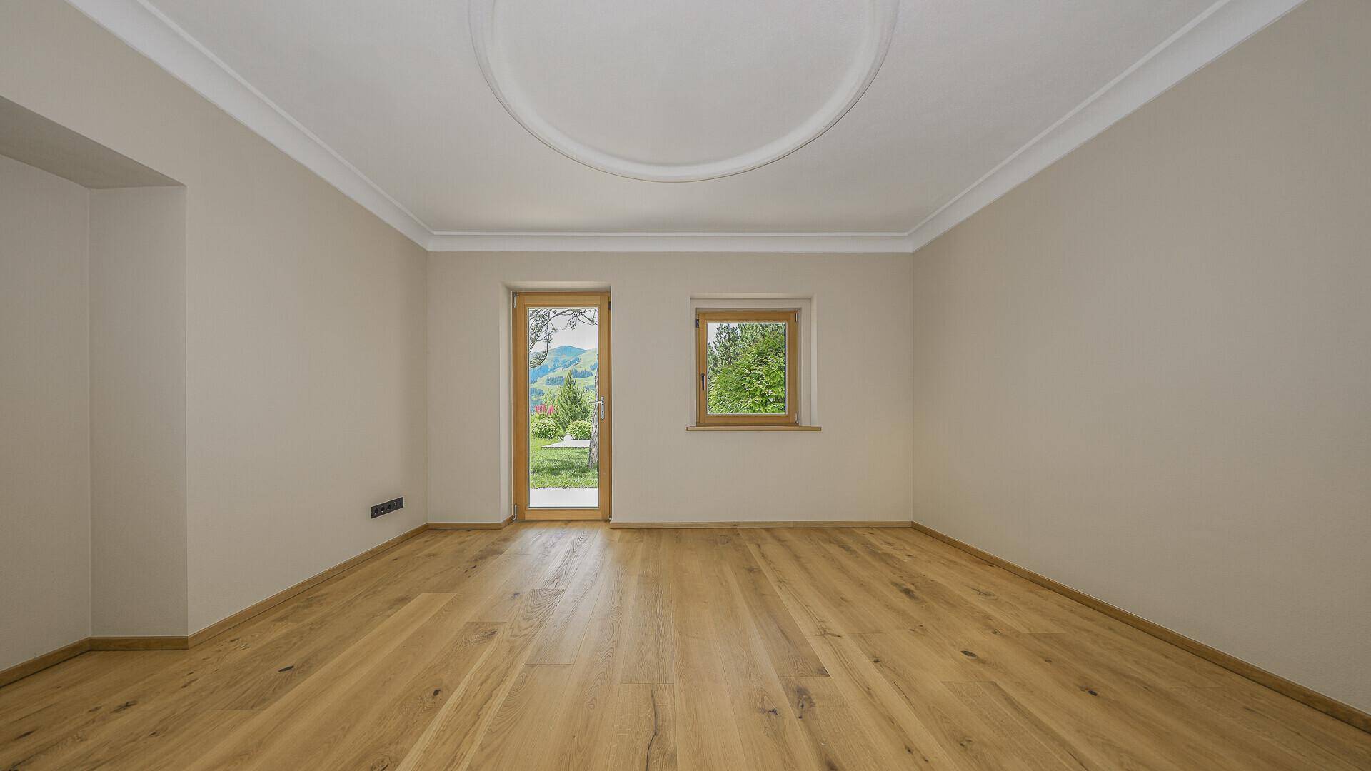 Heller Raum mit Parkettboden, Stuckdecke und Zugang zum Garten.