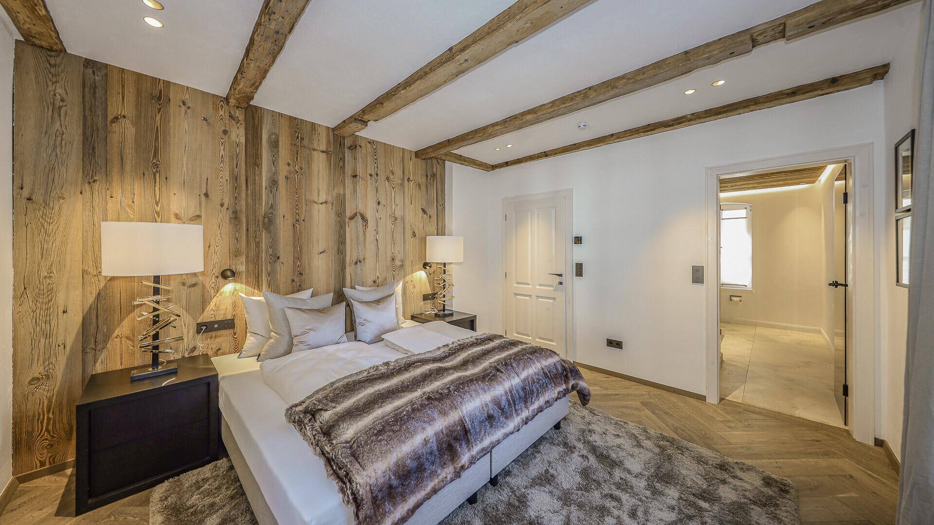 Schlafzimmer im alpinen Stil mit Holzwand, sichtbaren Balken und Parkettboden.