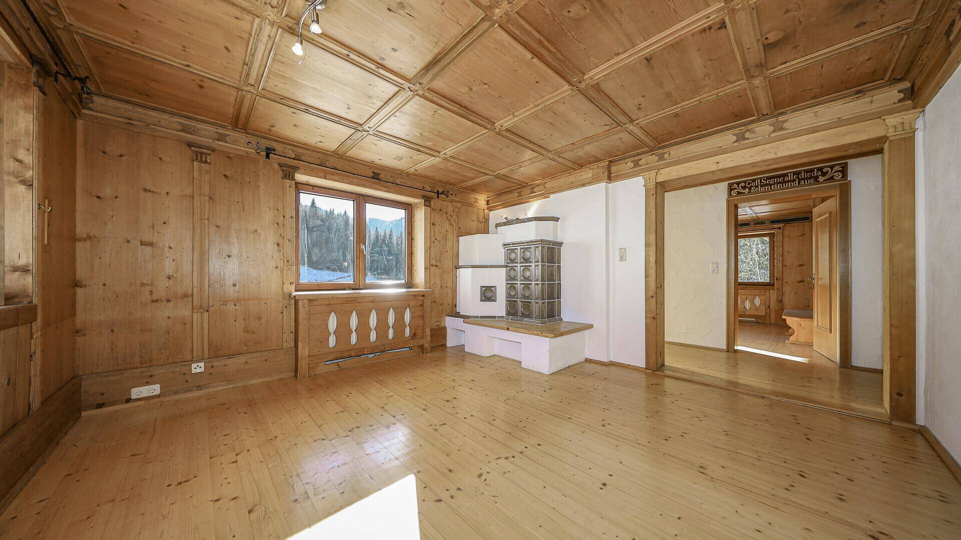 Traditionelles Wohnzimmer mit Holzvertäfelung, Kachelofen und Blick auf die Berge.