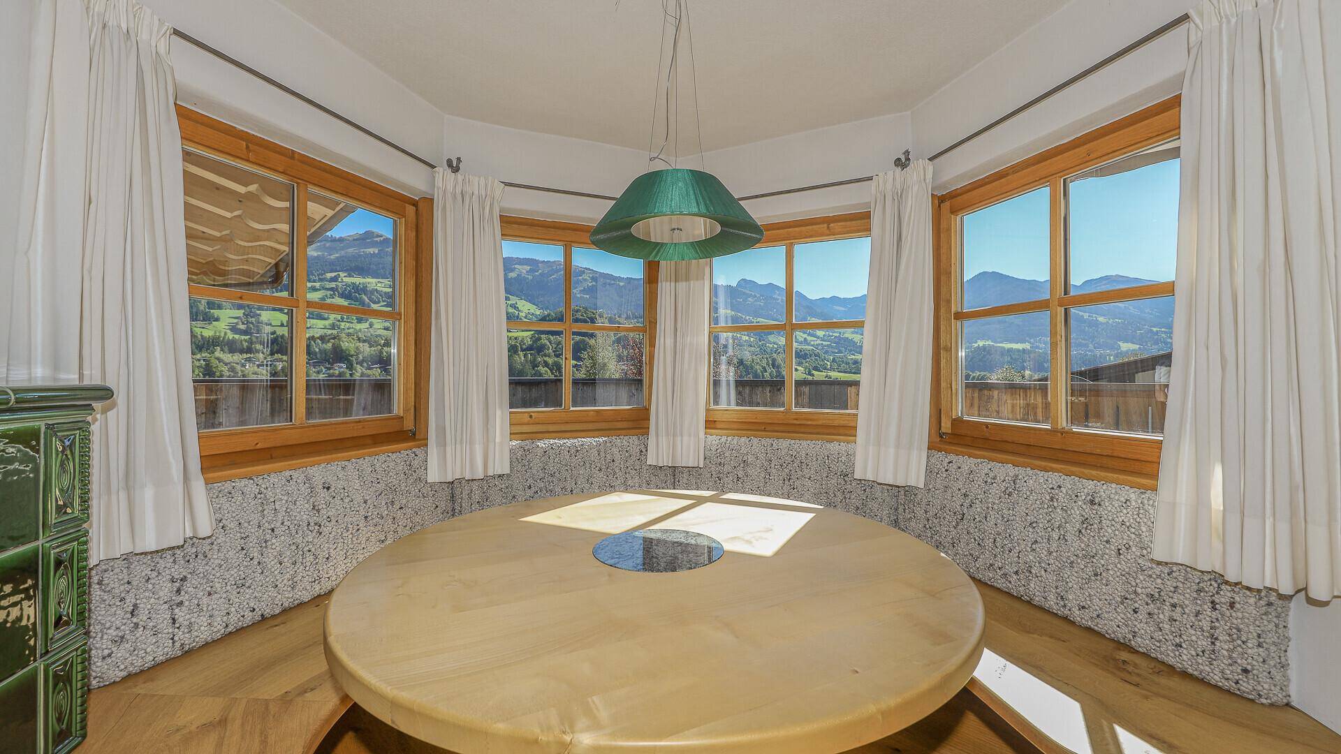 Heller Essbereich mit rundem Holztisch und Sitzbank, umgeben von Fenstern mit Bergblick.