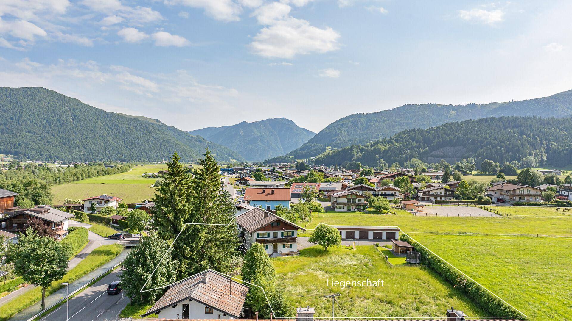 Luftaufnahme des Grundstücks an einer Straße, umgeben von Natur und alpiner Landschaft.