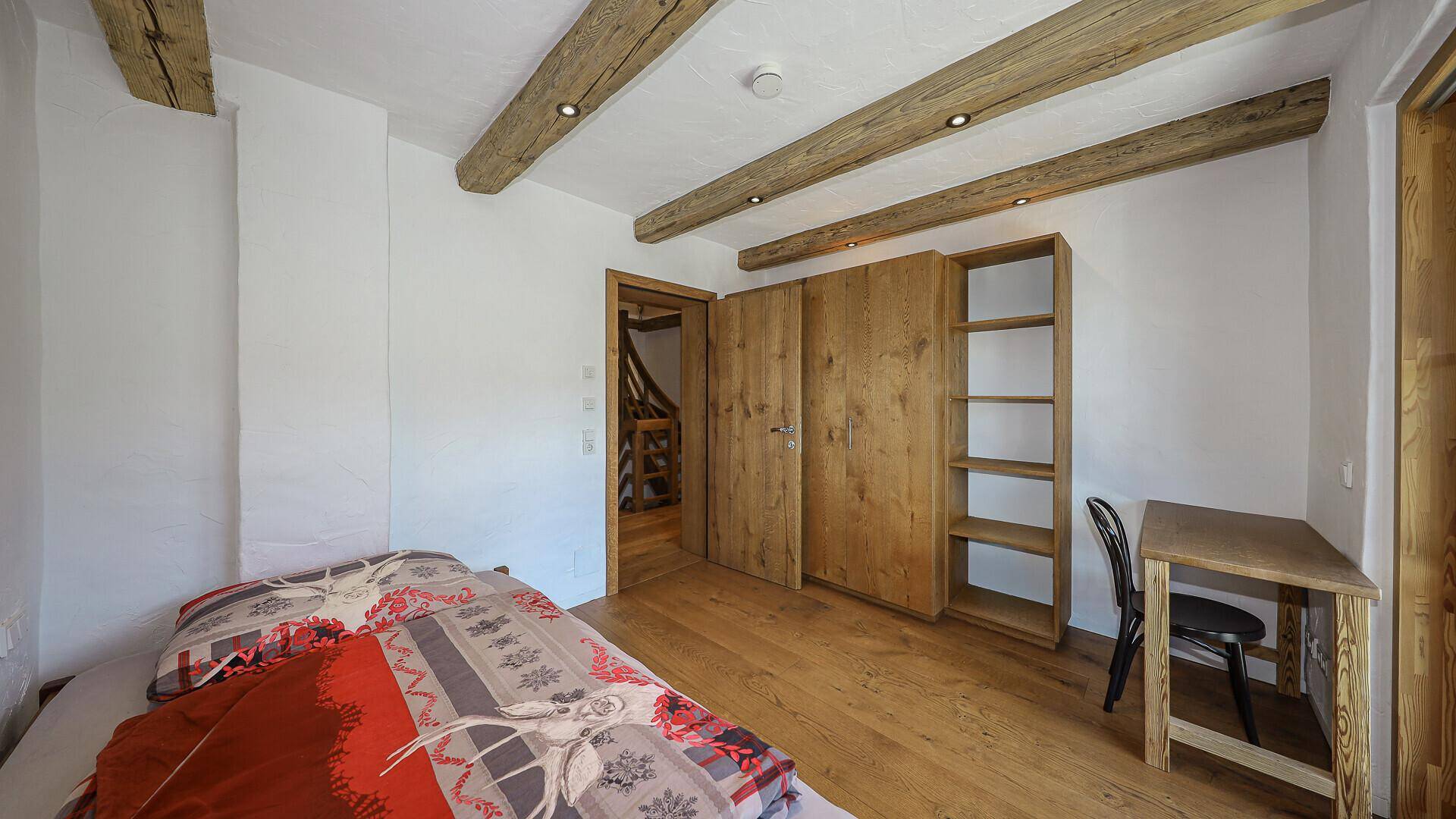 Schlafzimmer mit Holzbalken, Parkettboden und offenem Holzregal.