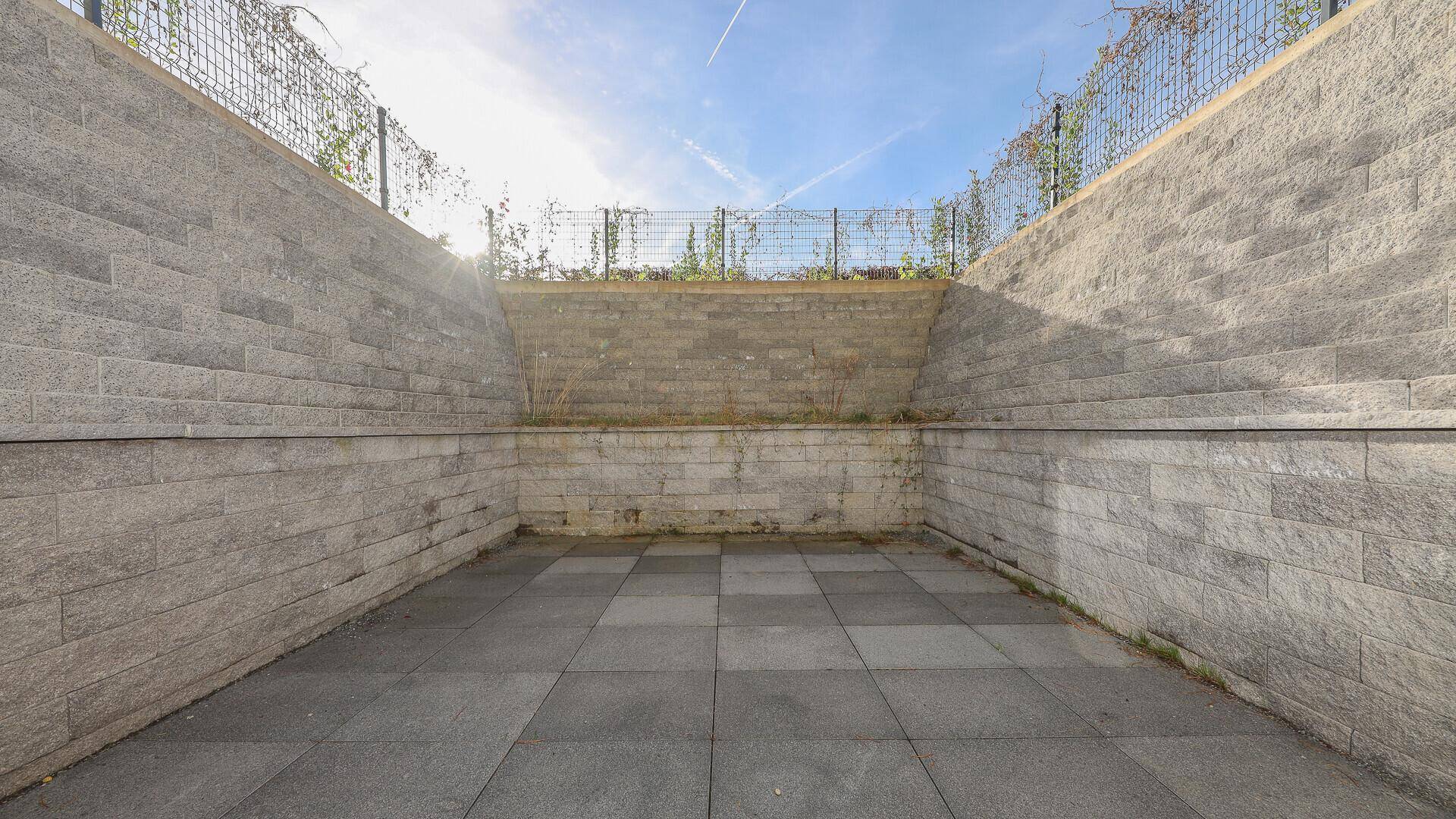 Leerer Innenhof mit Steinwänden und Fliesenboden, bereit für individuelle Gestaltung.