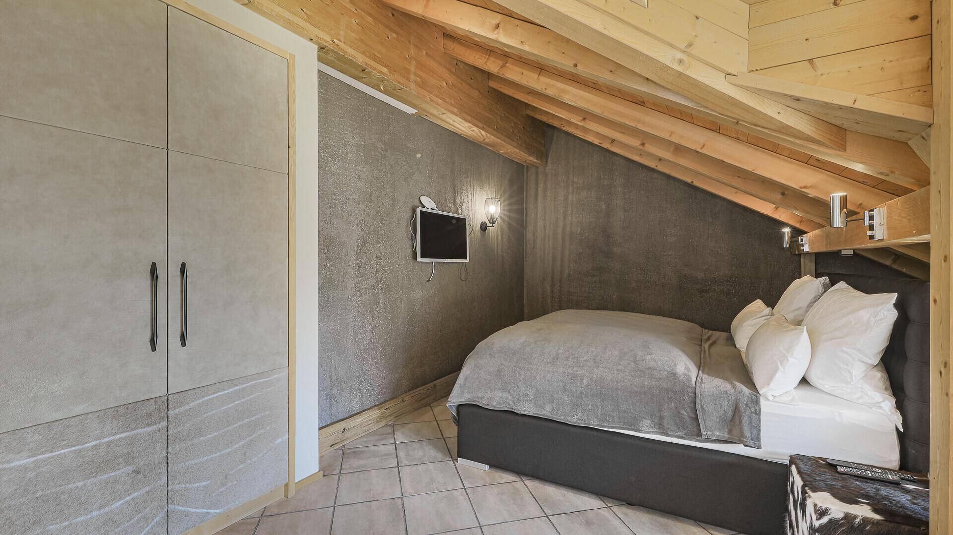 Dachschlafzimmer mit Holzbalken, Einbauschrank und gemütlichem Bett unter der Dachschräge.