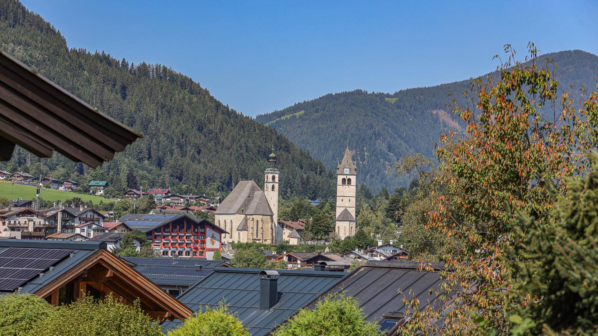 Malerischer Blick auf ein Bergdorf mit Kirche und grünen Hügeln im Hintergrund.