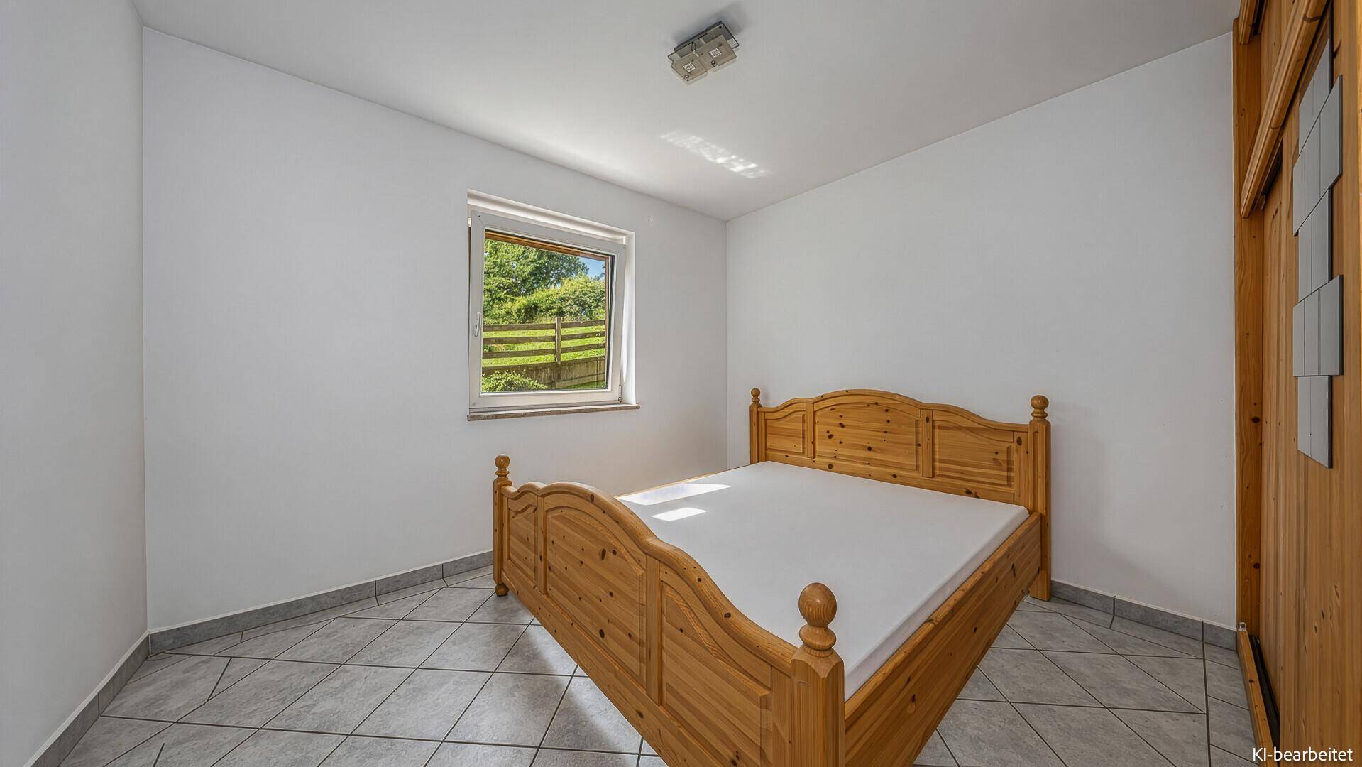 Helles Schlafzimmer mit Fliesenboden und traditionellem Holzbett, mit Fenster zum Garten.