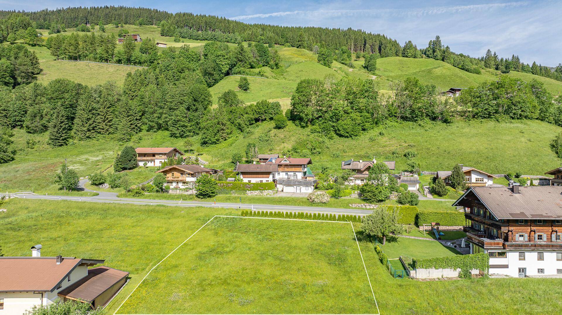 Weitläufiges grünes Grundstück in einer malerischen Berglandschaft, umgeben von Bäumen und Häusern.