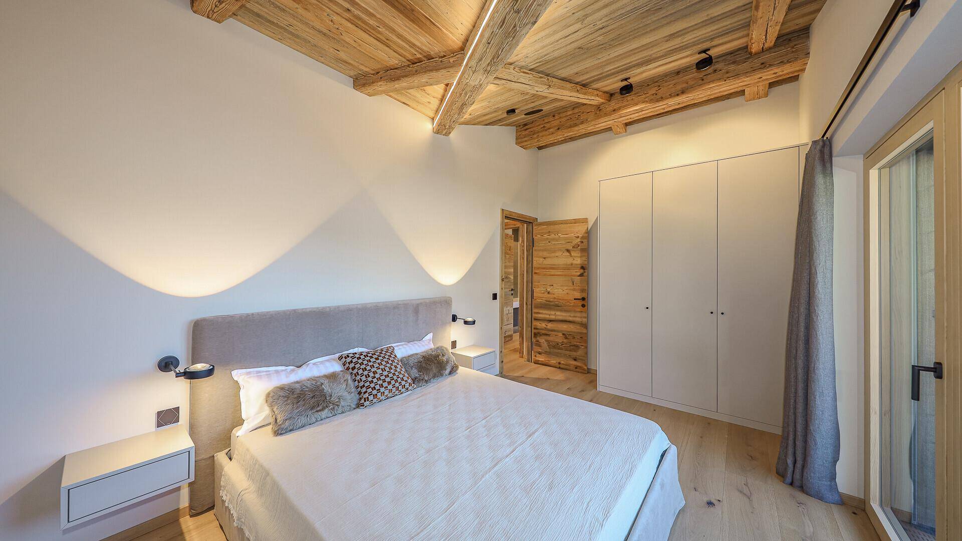 Gemütliches Schlafzimmer mit Holzbalkendecke, Einbauschränken und modernem Bett.