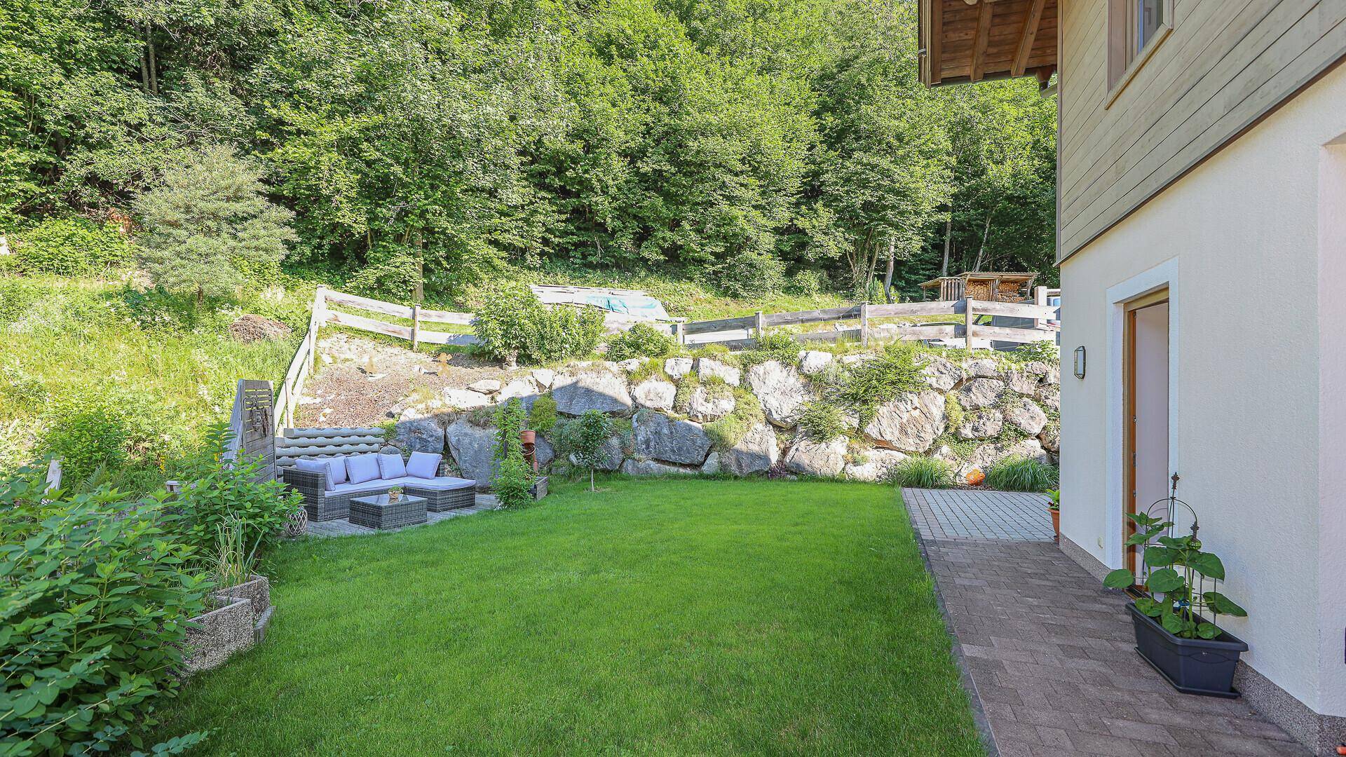 Ruhiger Gartenbereich mit Rasen, Steinterrasse und gemütlicher Lounge-Ecke am Hang.