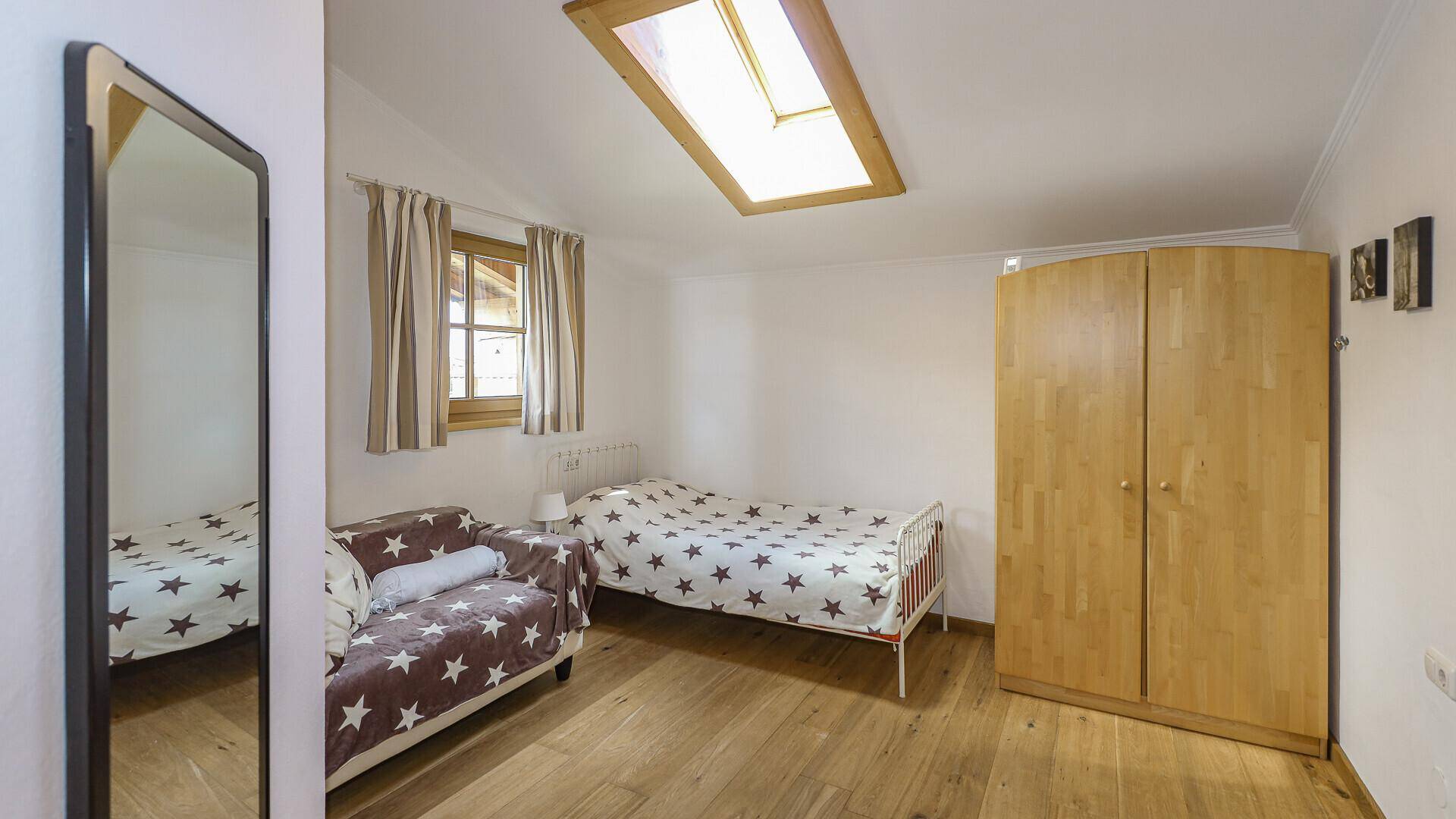 Gemütliches Schlafzimmer mit Einzelbett, Sofa, Holzschrank und Dachfenster.